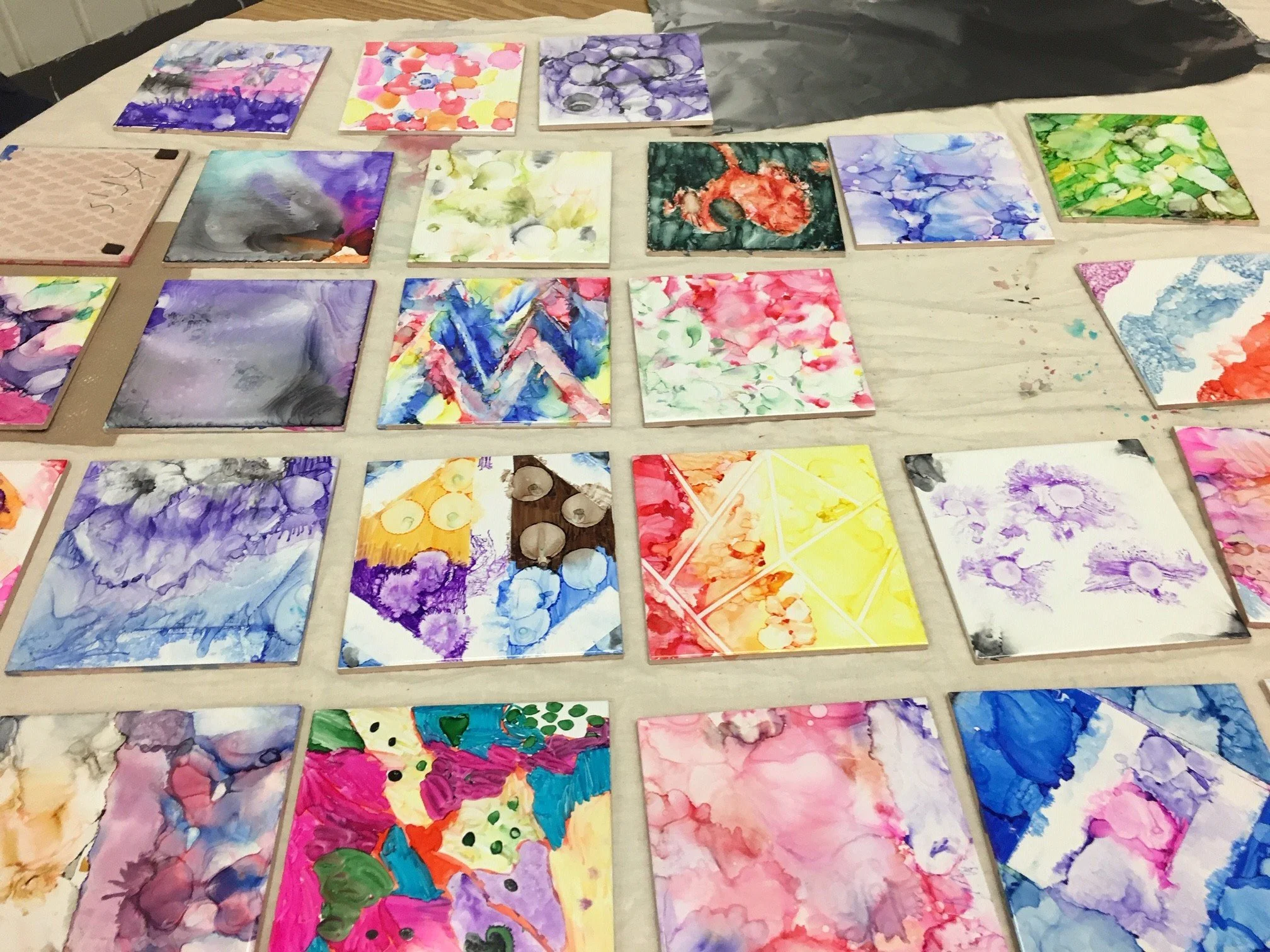 Collection of small, colorful abstract watercolor paintings arranged on a large table.