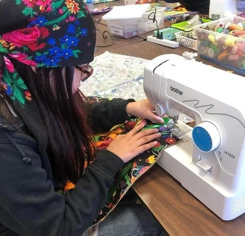 Person sewing fabric with a Brother sewing machine at a craft table with various sewing supplies.