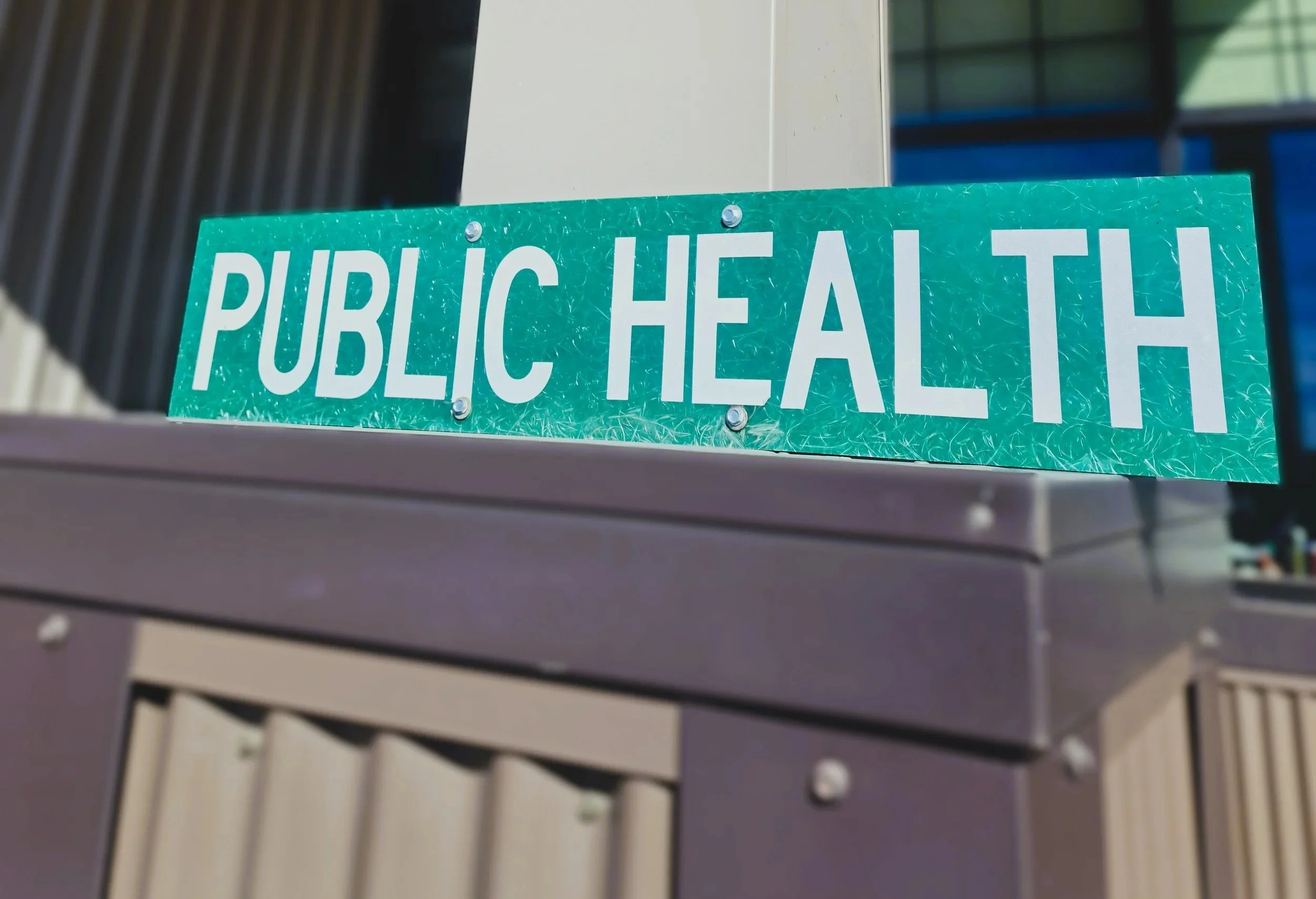 Green street sign reading 'Public Health' attached to a pole in an urban area.