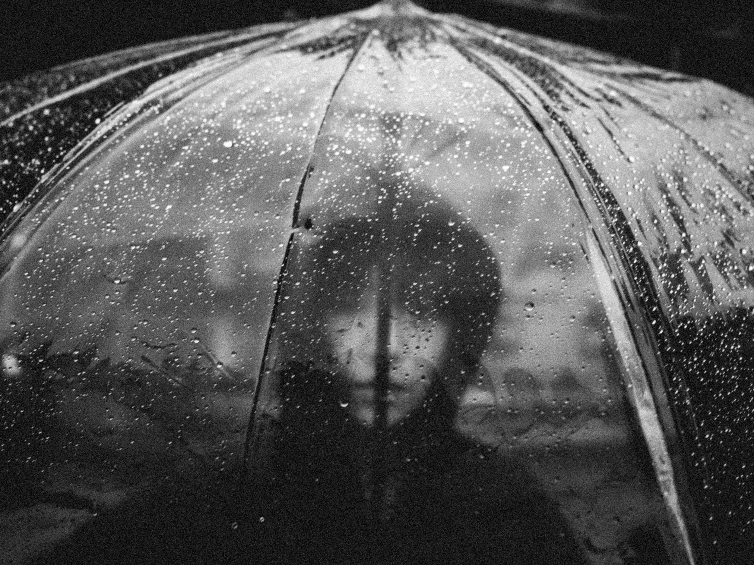 Close-up of a transparent umbrella covered with raindrops at night, with a blurred dark background and faint reflections.