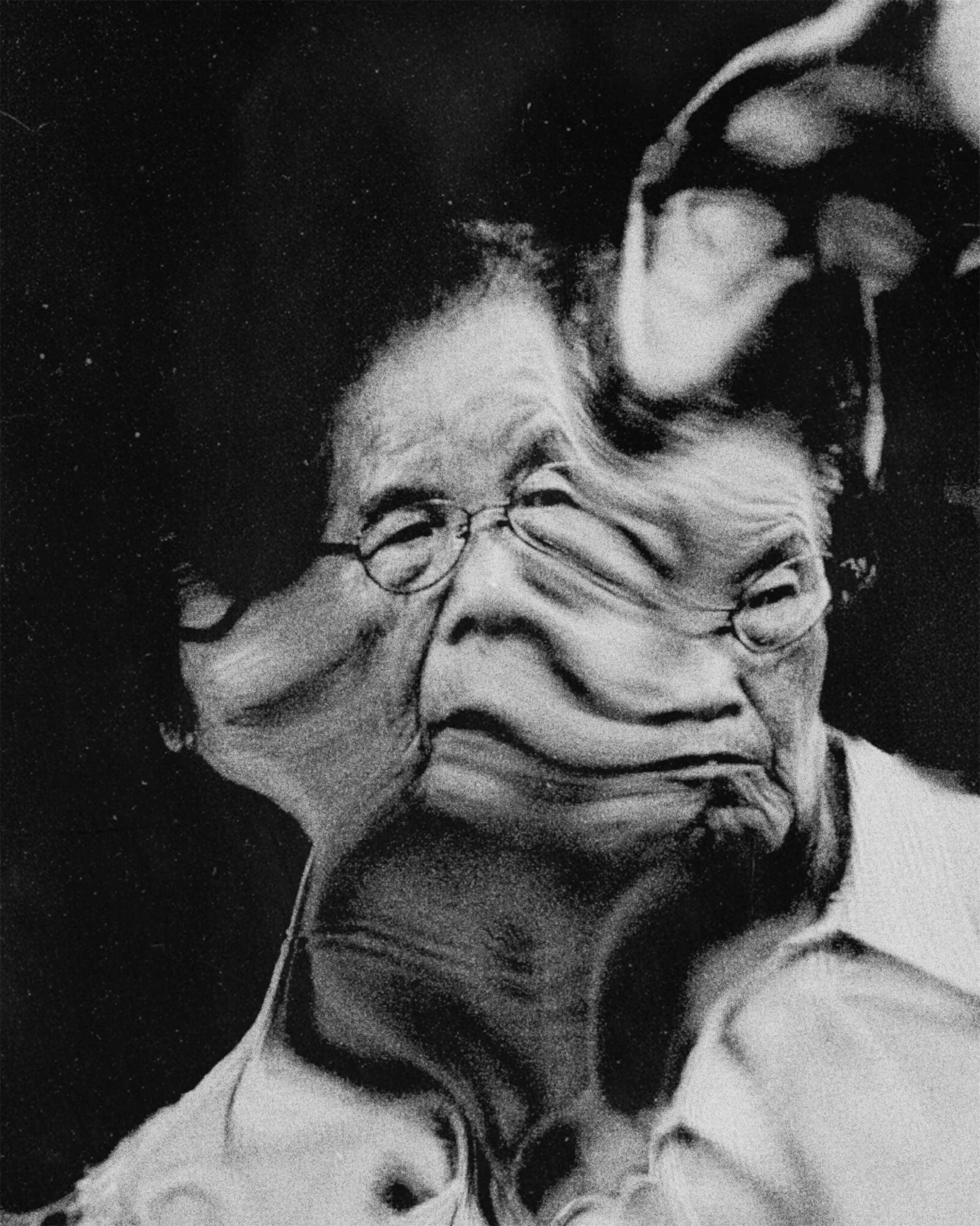 Black and white low-resolution photo of a person with glasses smiling and covering part of their face with their hand, with an afro hairstyle, listening to music with earphones.