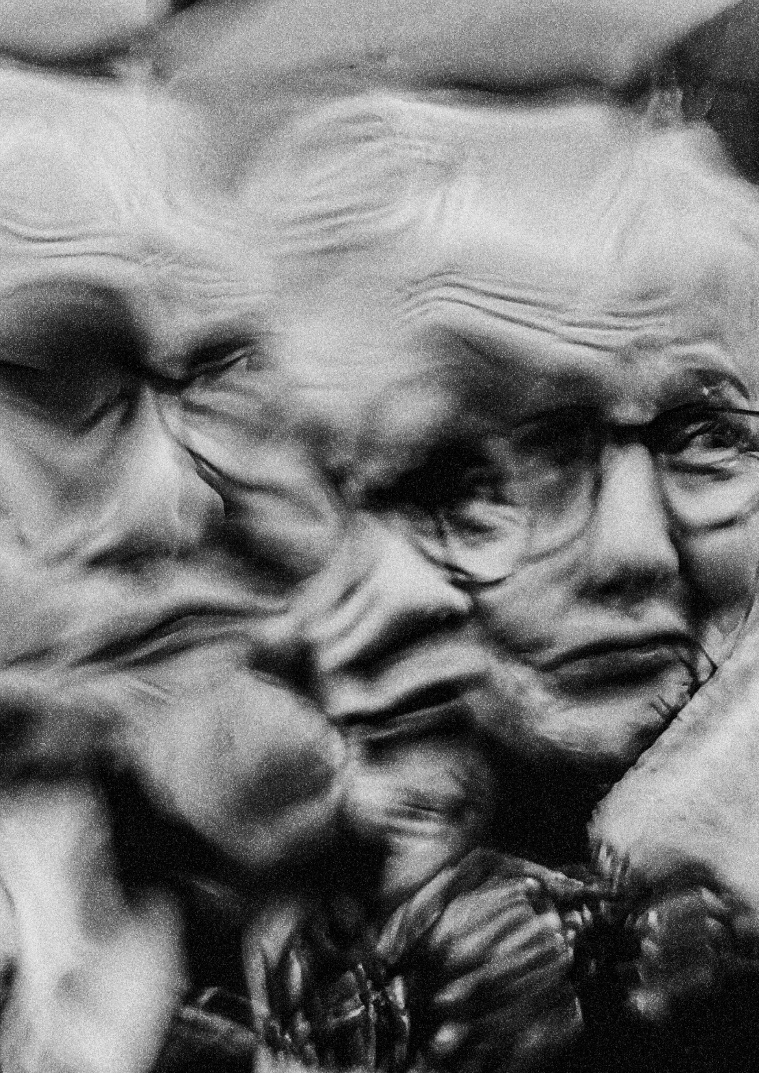 Close-up black and white photo of a face with a wide smile showing teeth, and curly hair.
