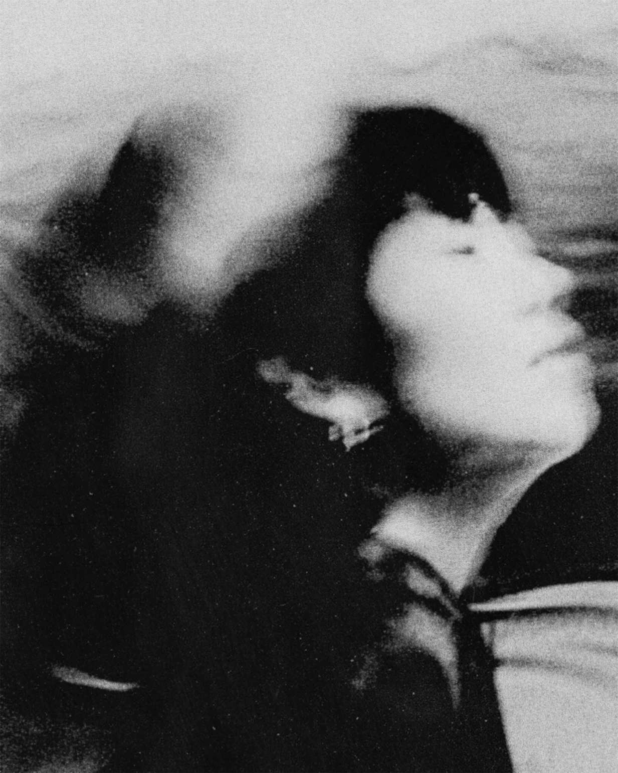 Black and white photo of a person with short hair resting their head on someone else's shoulder, both facing away from the camera.