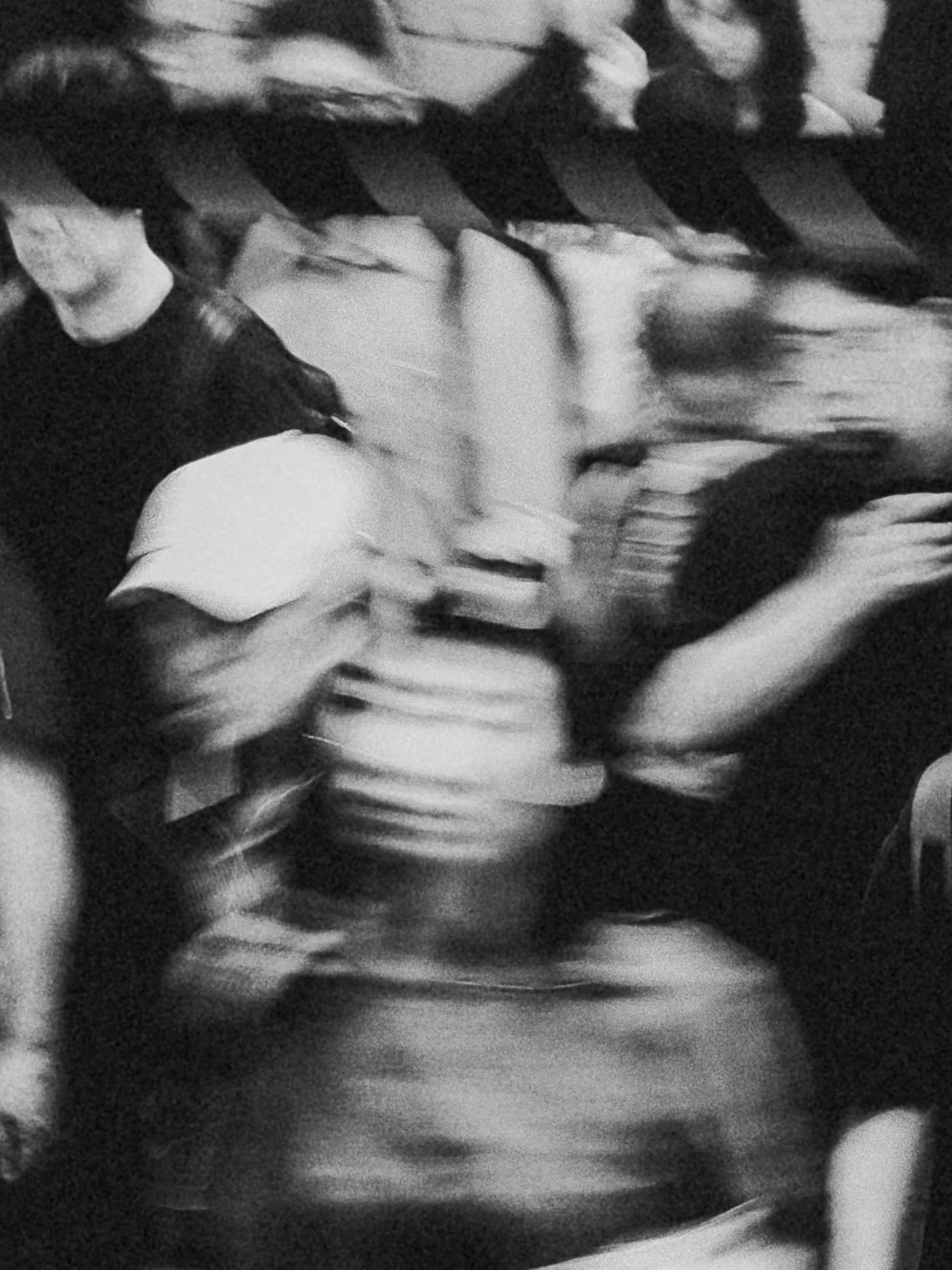 Blurry black and white photo of a group of people. One person is holding a bottle, while others are standing close in a crowded setting.