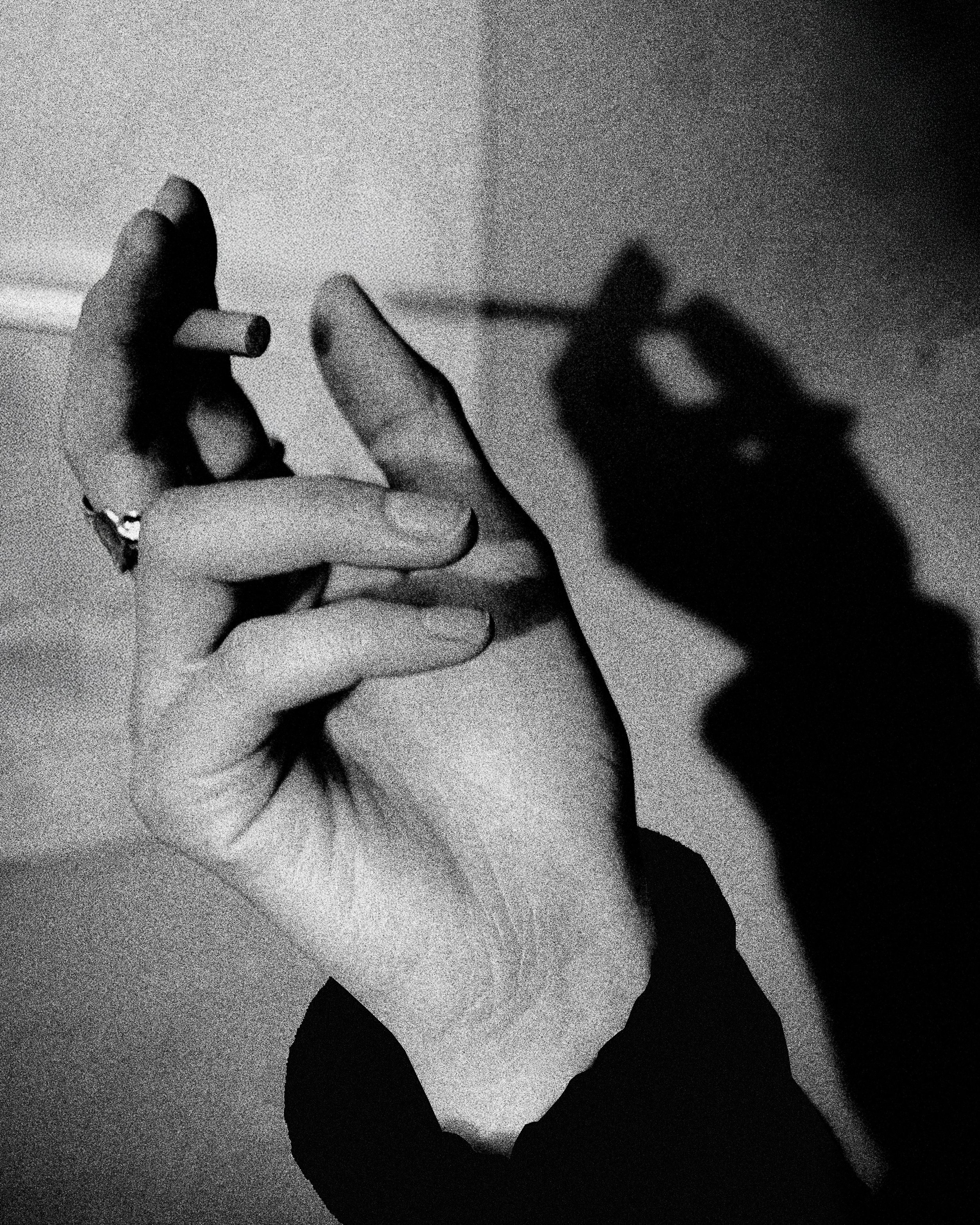 A black and white silhouette of an open flower with a person holding a cigarette, creating the shadow of a person holding a cigarette with a distinctive beard in the background.