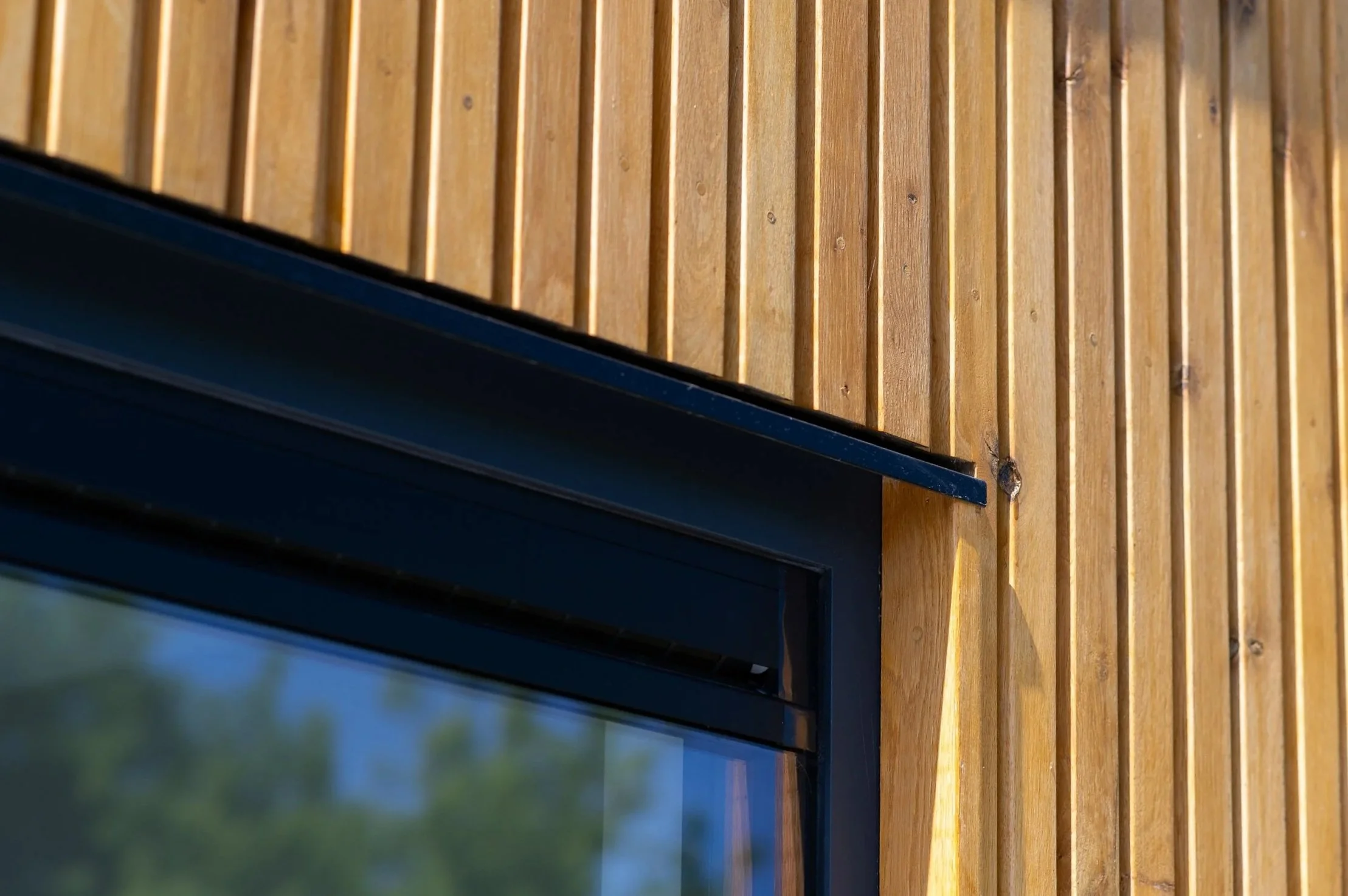 Een close-up van een raam met een zwarte kozijn, bevestigd aan een muur bekleed met verticale houten planken.