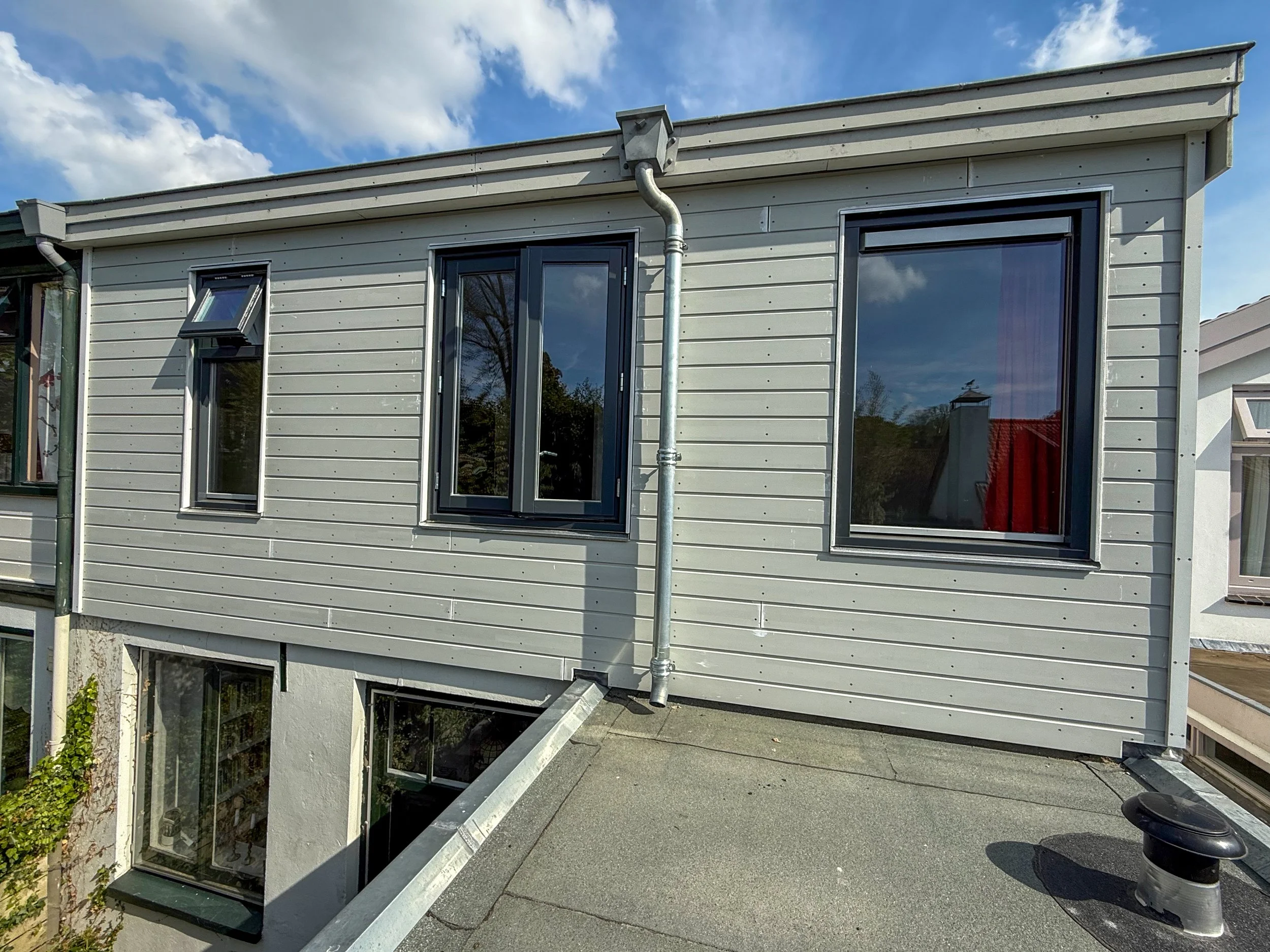 Bovenverdieping van een modern huis met drie grote ramen en een blauw hemel met wolken op de achtergrond.