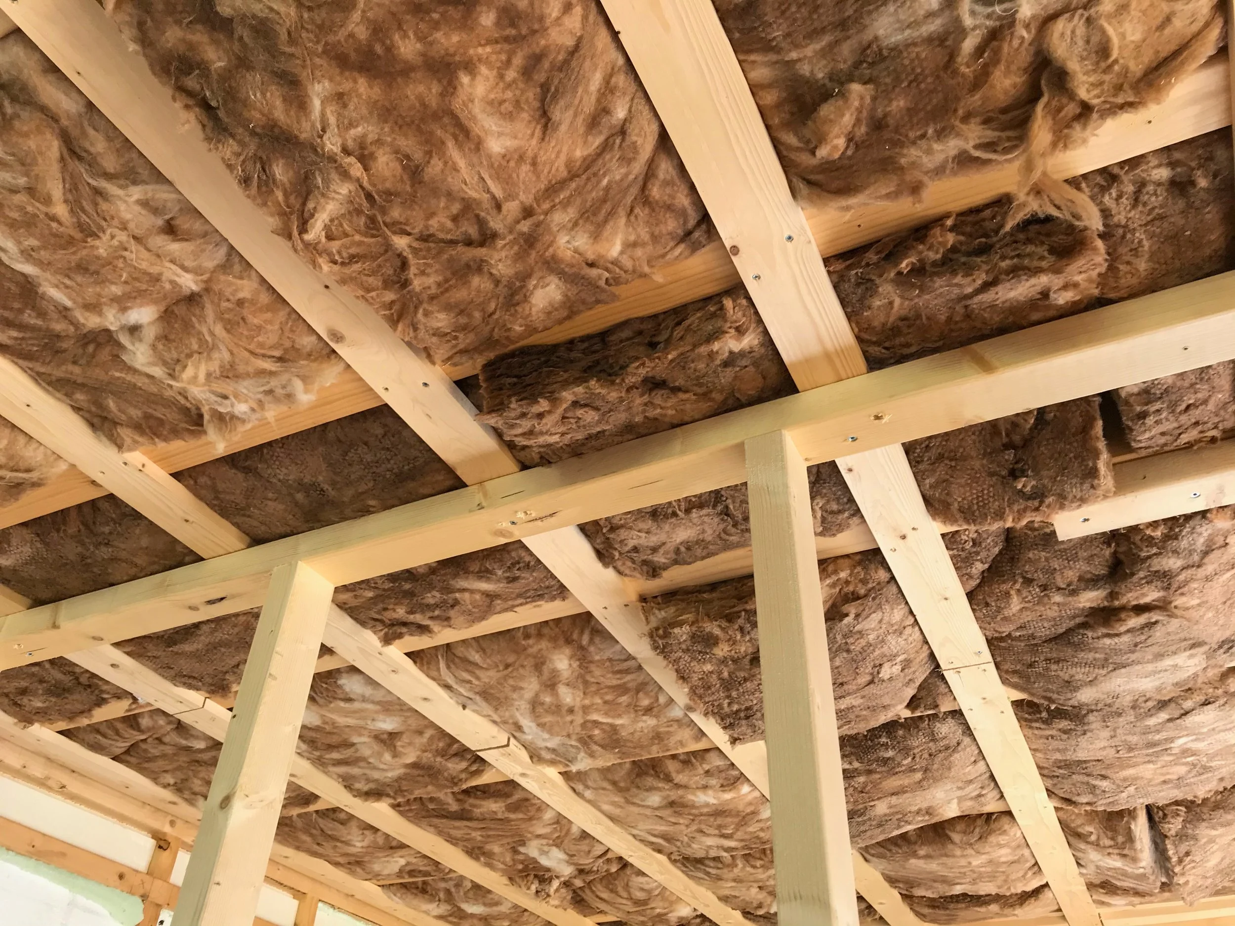 Isolatiemateriaal aangebracht tussen houten plafondconstructie.