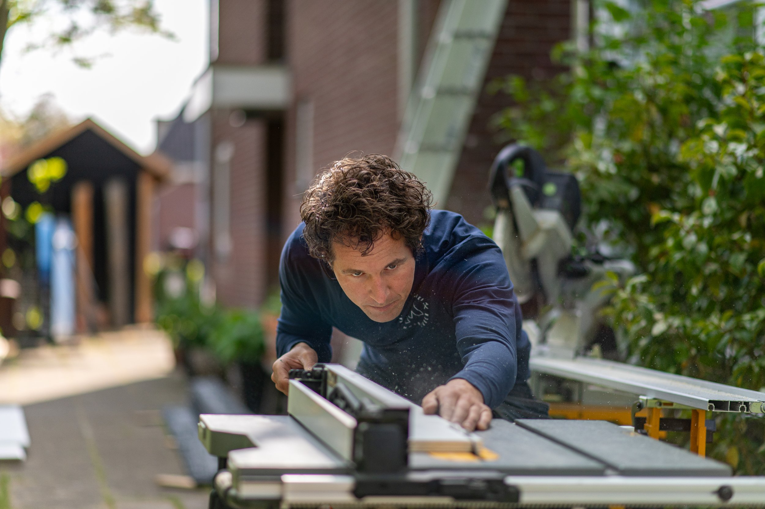 Een man die op knieën een afwerkingswerk aan een plat dak doet met behulp van een elektrische zaag.