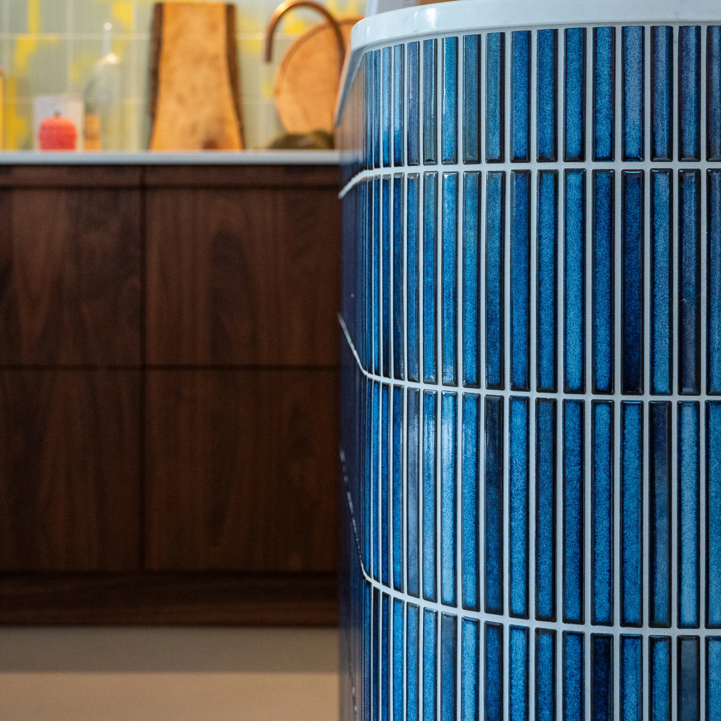 Close-up van een blauw luchtfilter van een apparaat, met een achtergrond van een houten meubel en decoratieve items.