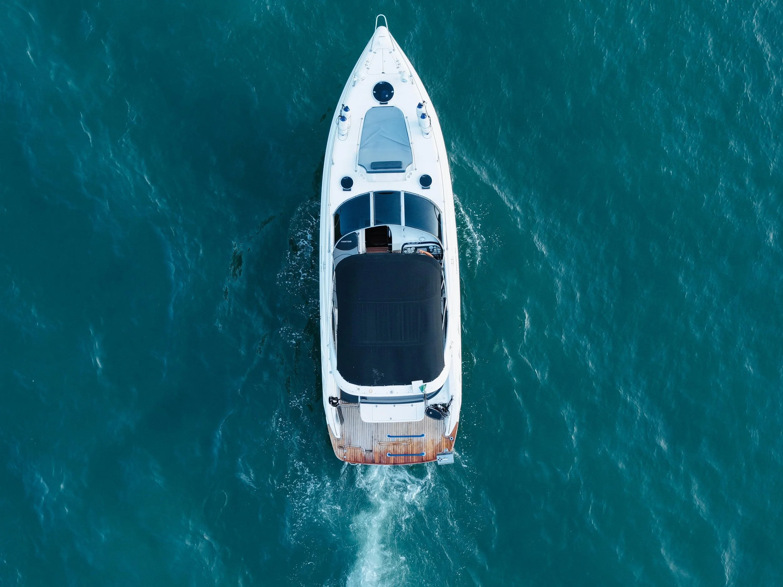 Top-down aerial view of a white yacht sailing on blue ocean water.