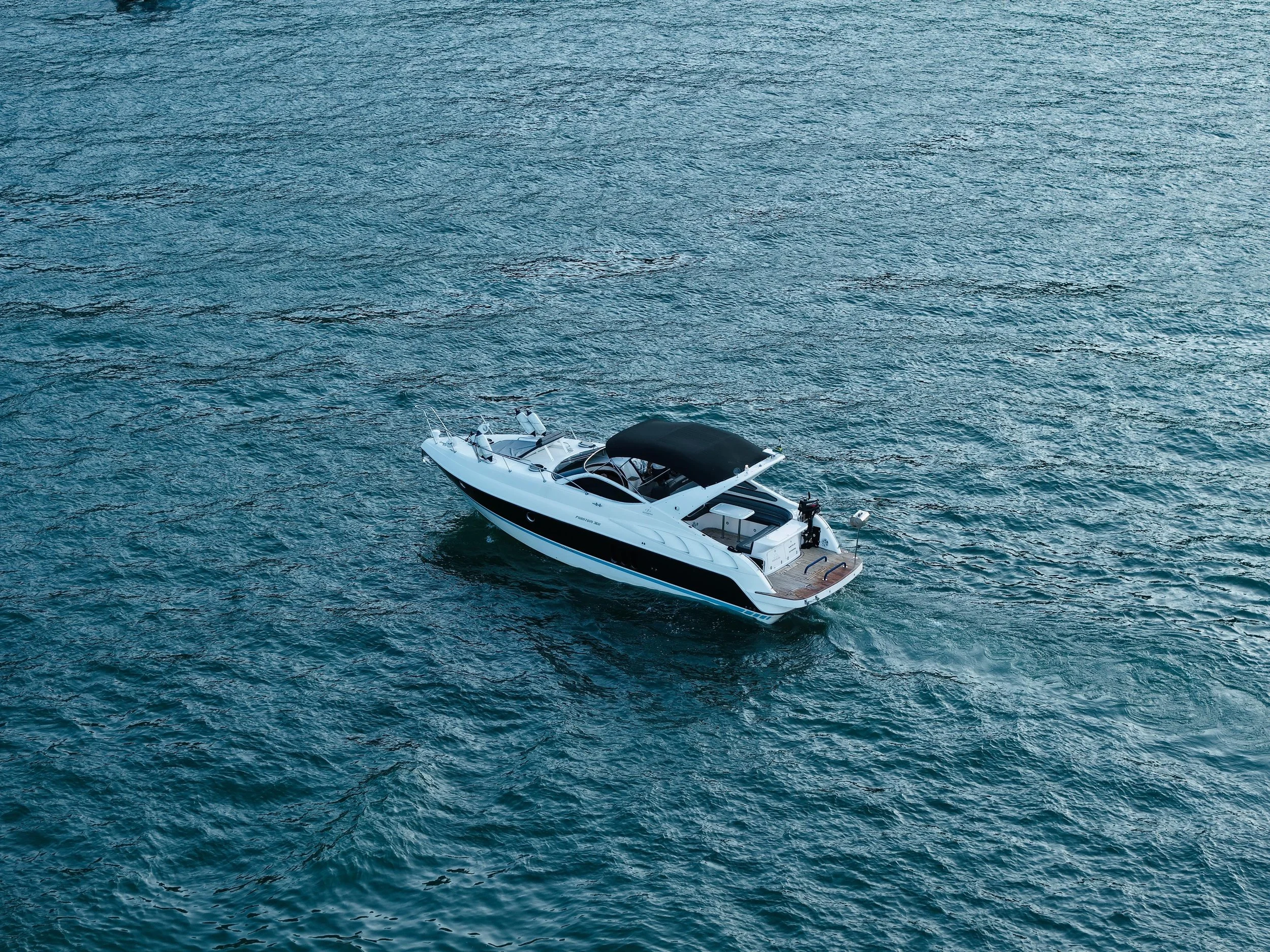 A white motorboat with a black canopy floating on a large body of water with visible ripples.