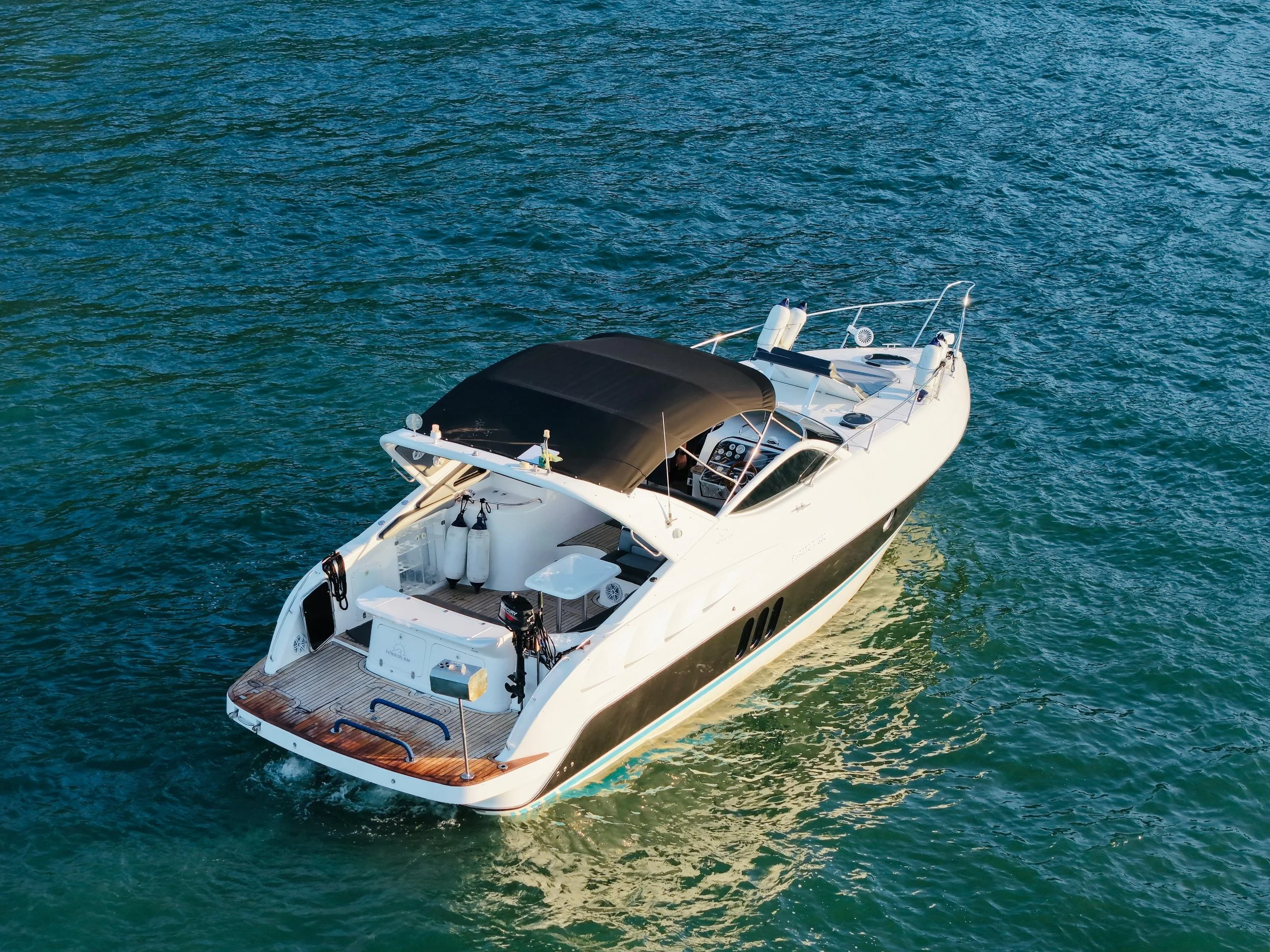 A white yacht sailing on blue-green water with a black sunshade on the upper deck.