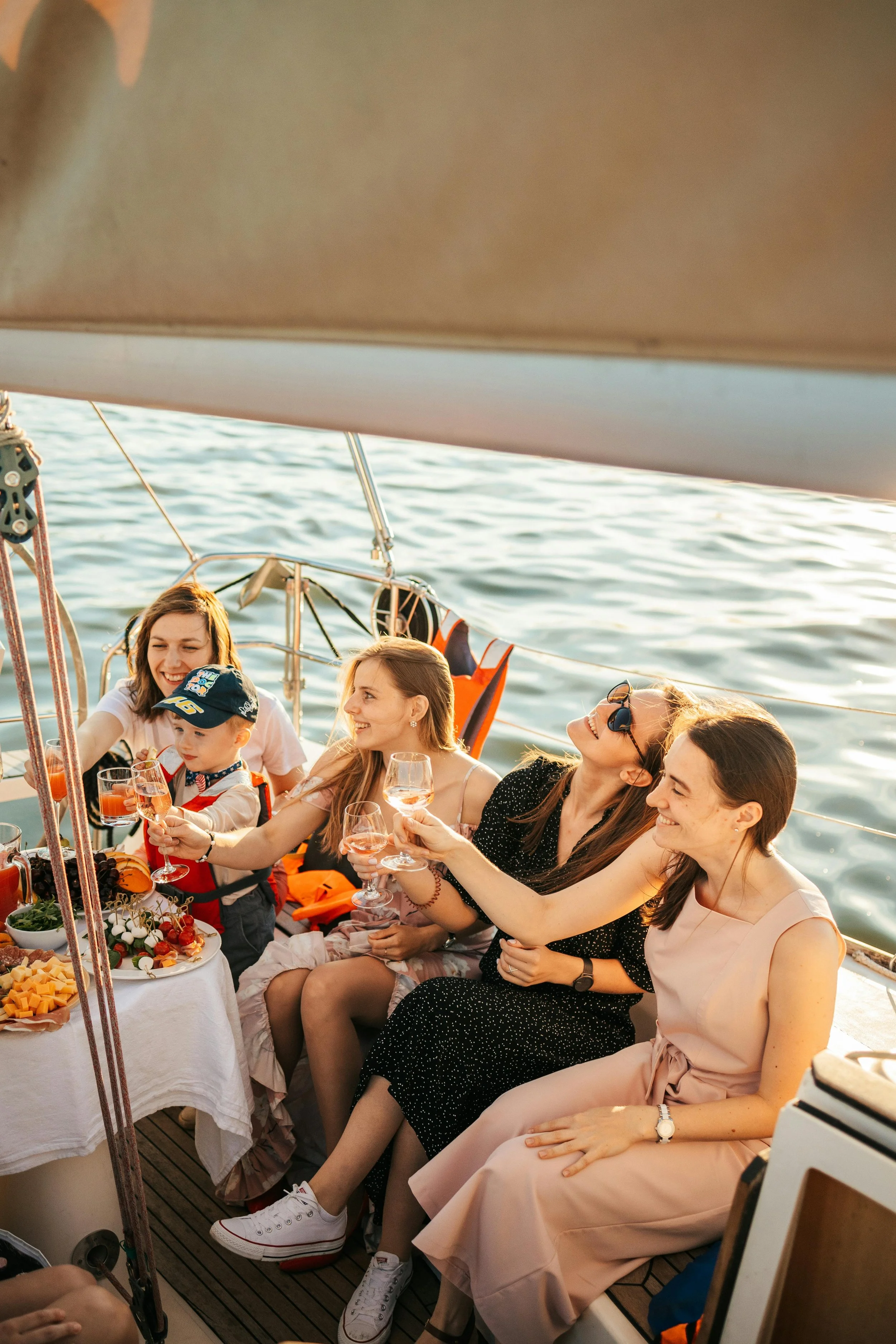 A group of women and children on a boat enjoying a meal, with water in the background during sunset.