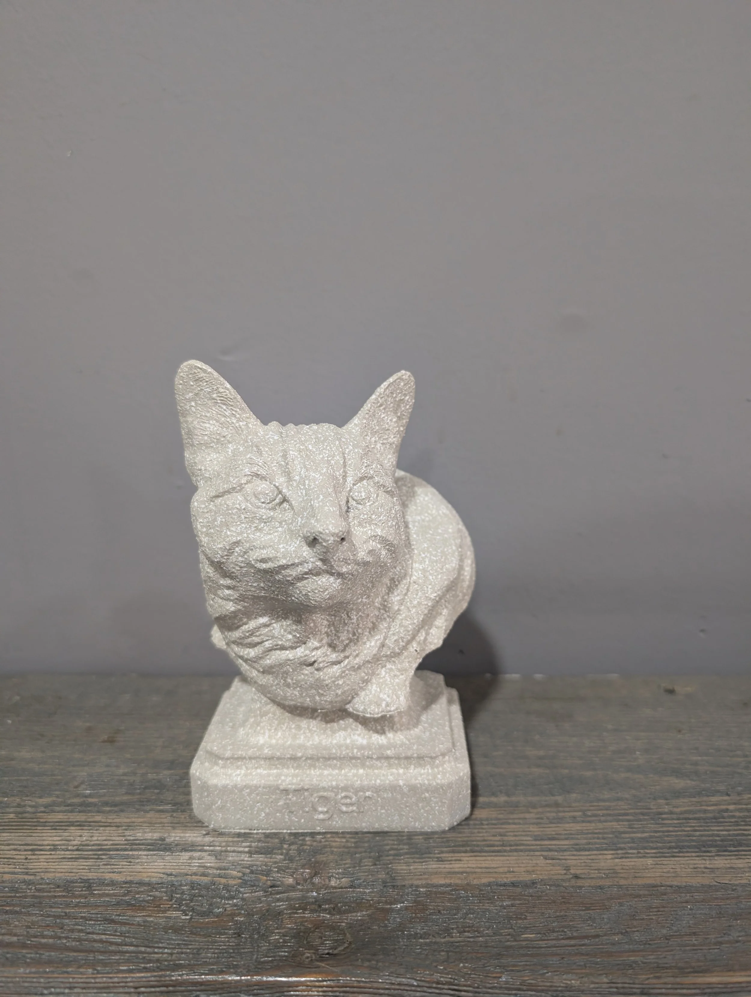 A decorative white cat figurine with a textured surface, sitting on a wooden surface against a gray background.