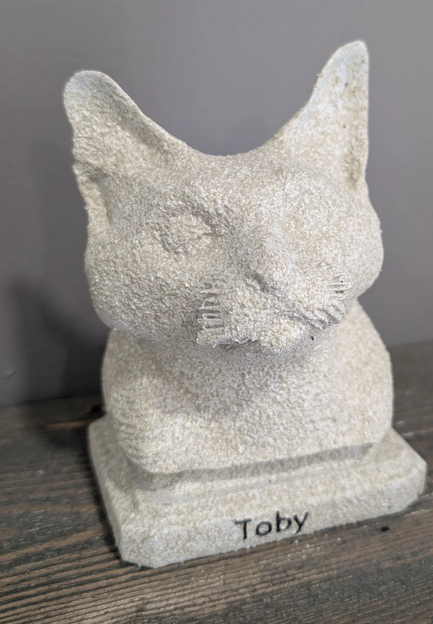 Sandstone cat figurine with the name Toby inscribed on the base, placed on a wooden surface.