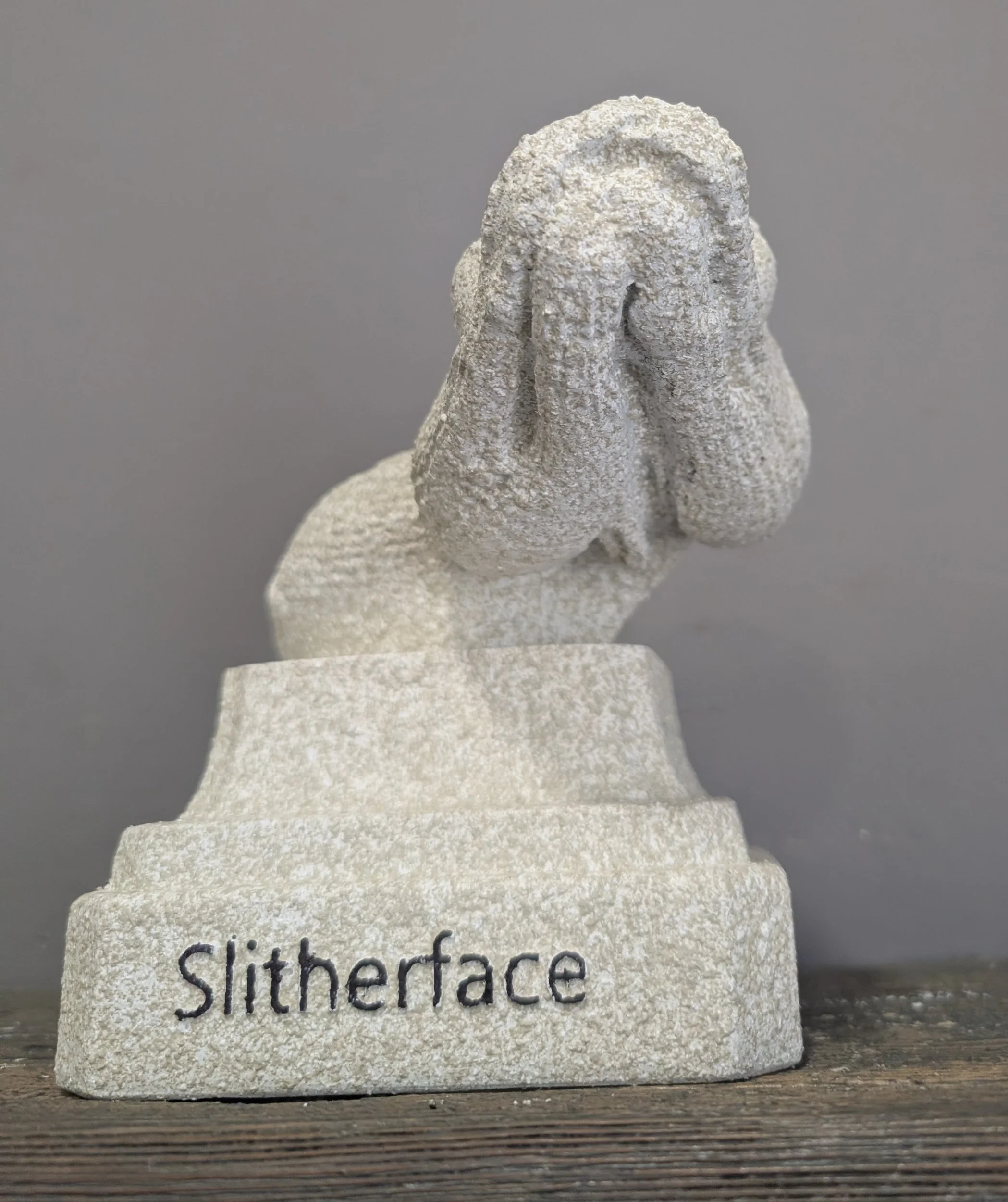 A stone sculpture with the face of a character covering its face with its hands, and the word 'Slithface' engraved on the base.