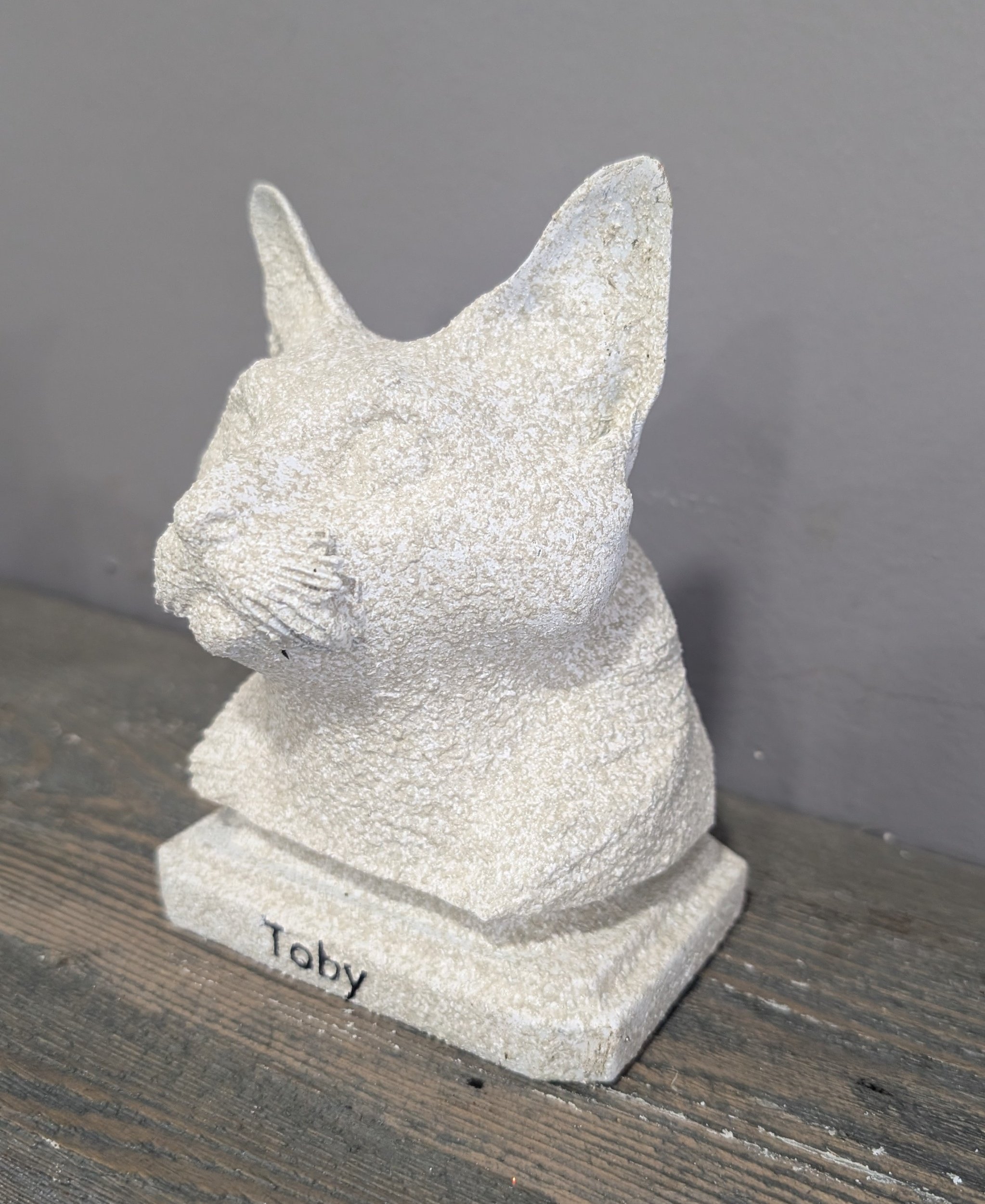 White stone figurine of a rabbit with the name 'Toby' engraved on the base, placed on a wooden surface against a gray background.