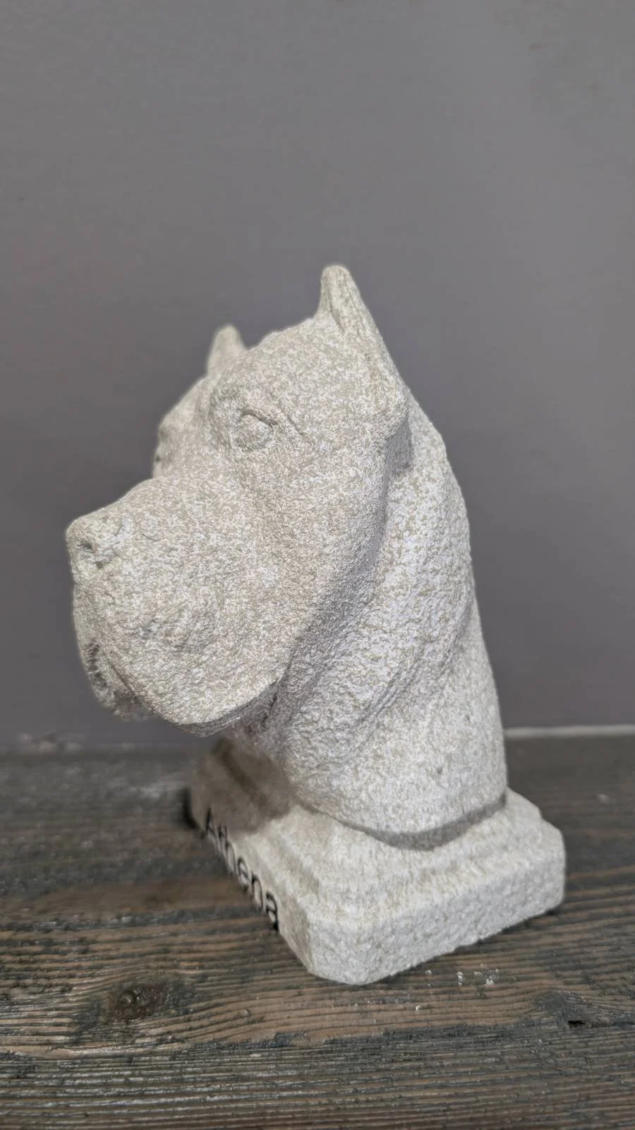 Stone sculpture of a horse's head on a wooden surface against a gray background.