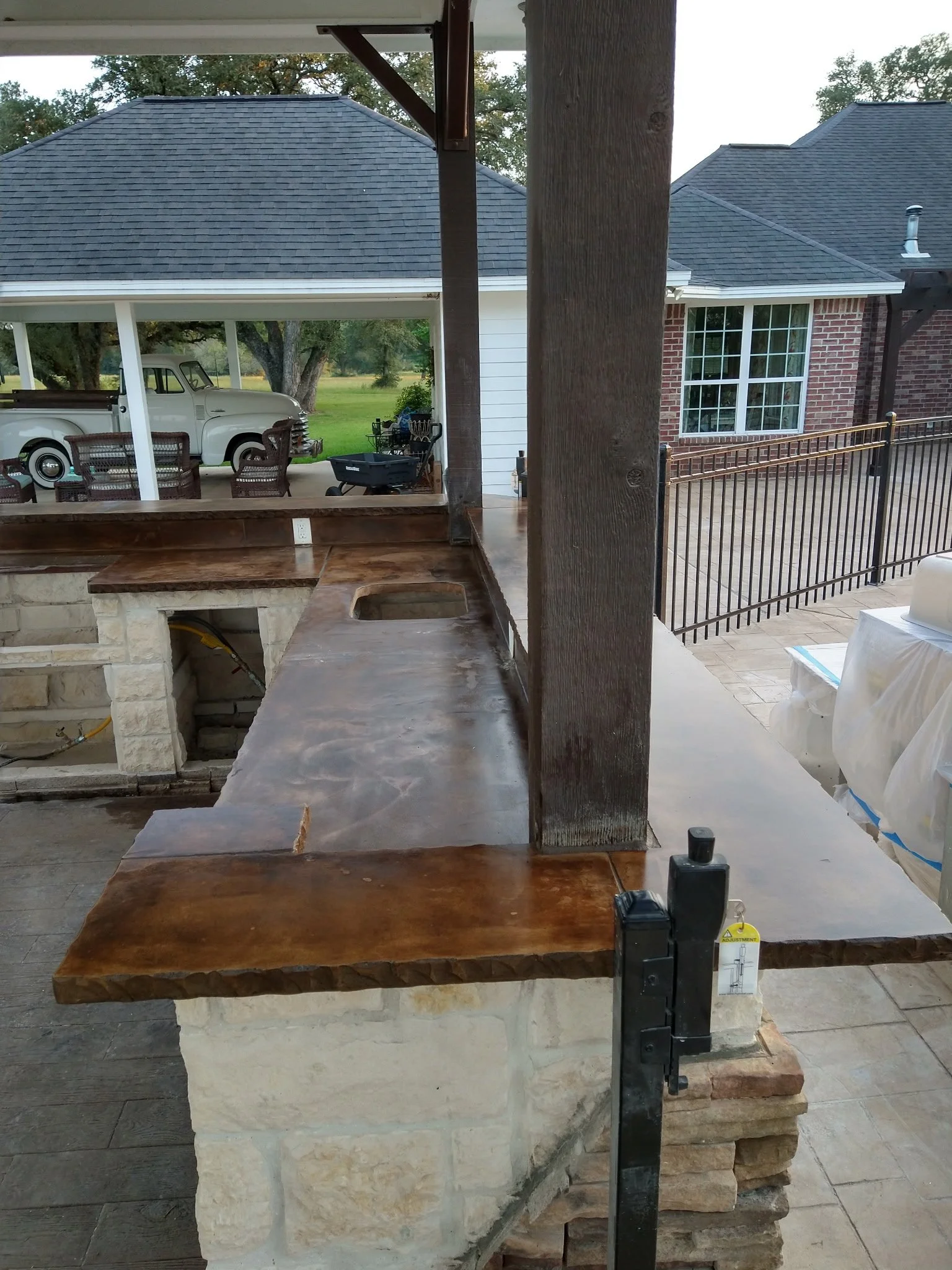 View of a backyard patio with a stone and wood countertop, a nearby patio area with a table and chairs, and a vintage truck parked under a covered area.