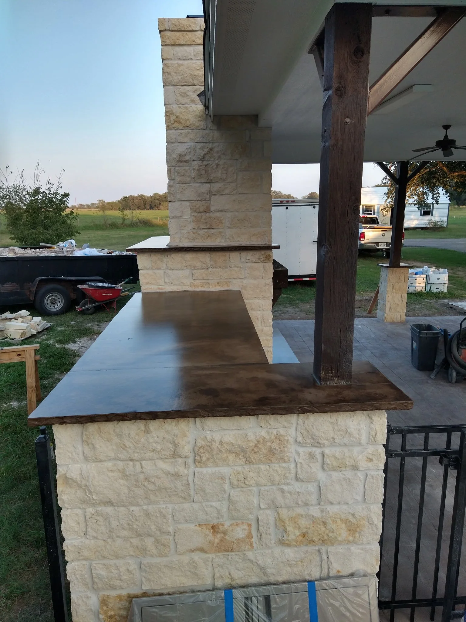 Close-up view of a stone and wood outdoor countertop with stone pillars in a backyard setting, under construction.