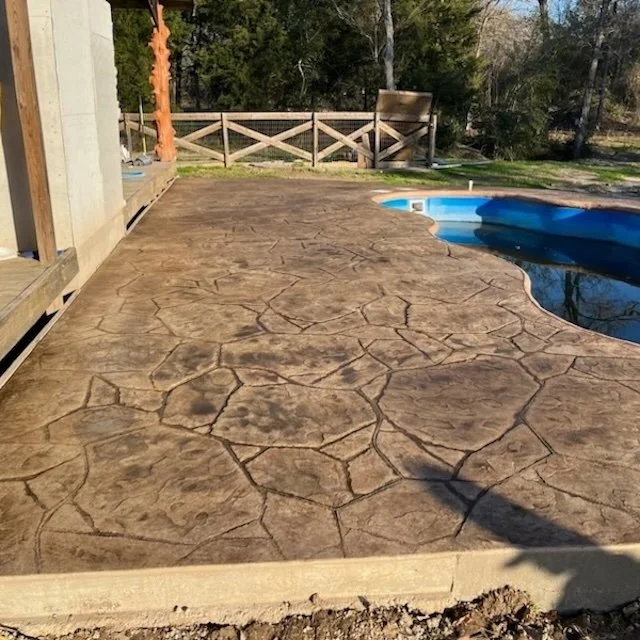 Concrete patio with decorative stamped pattern next to a swimming pool.