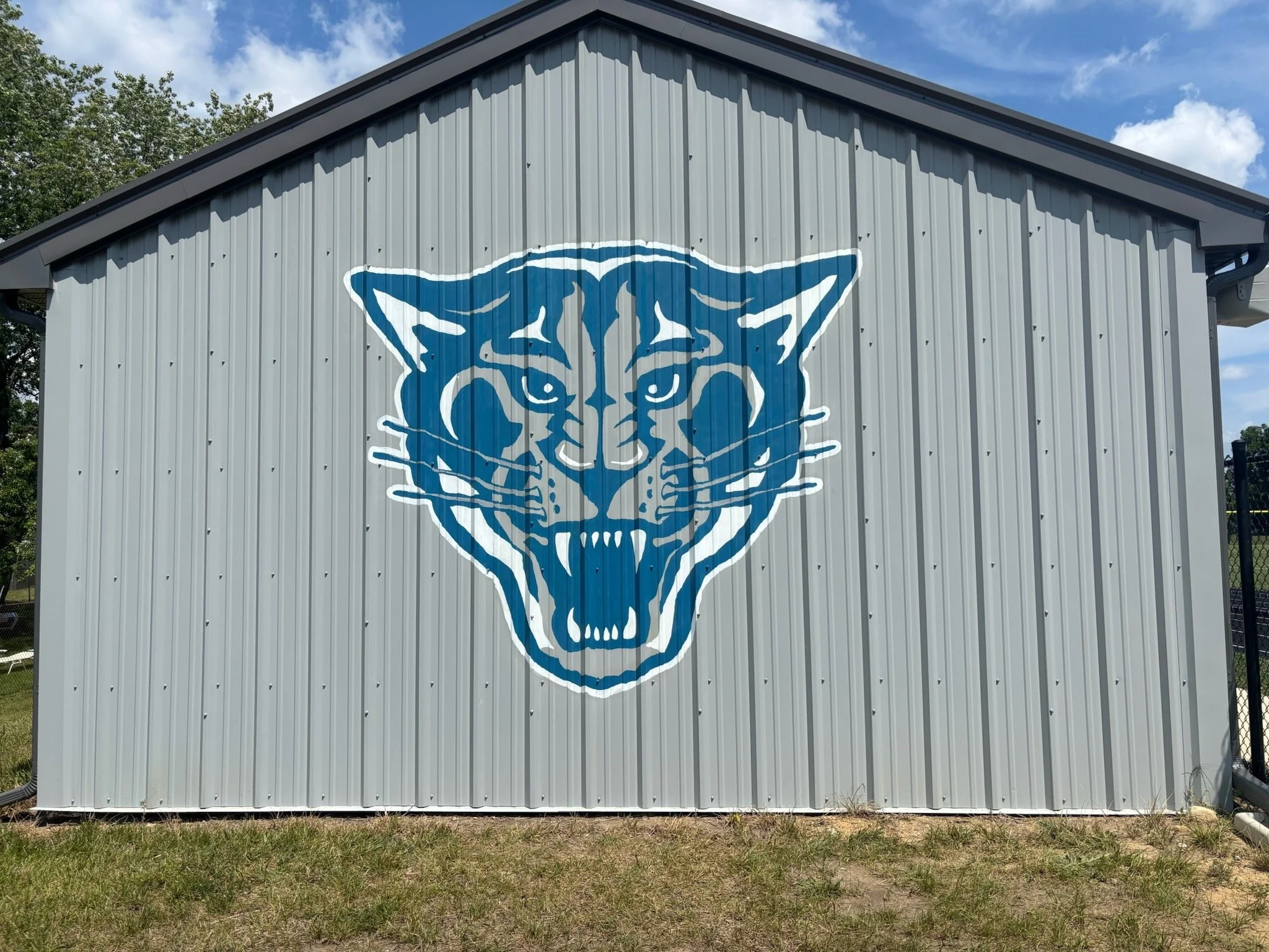 Large blue and white panther logo painted on the side of a corrugated metal building