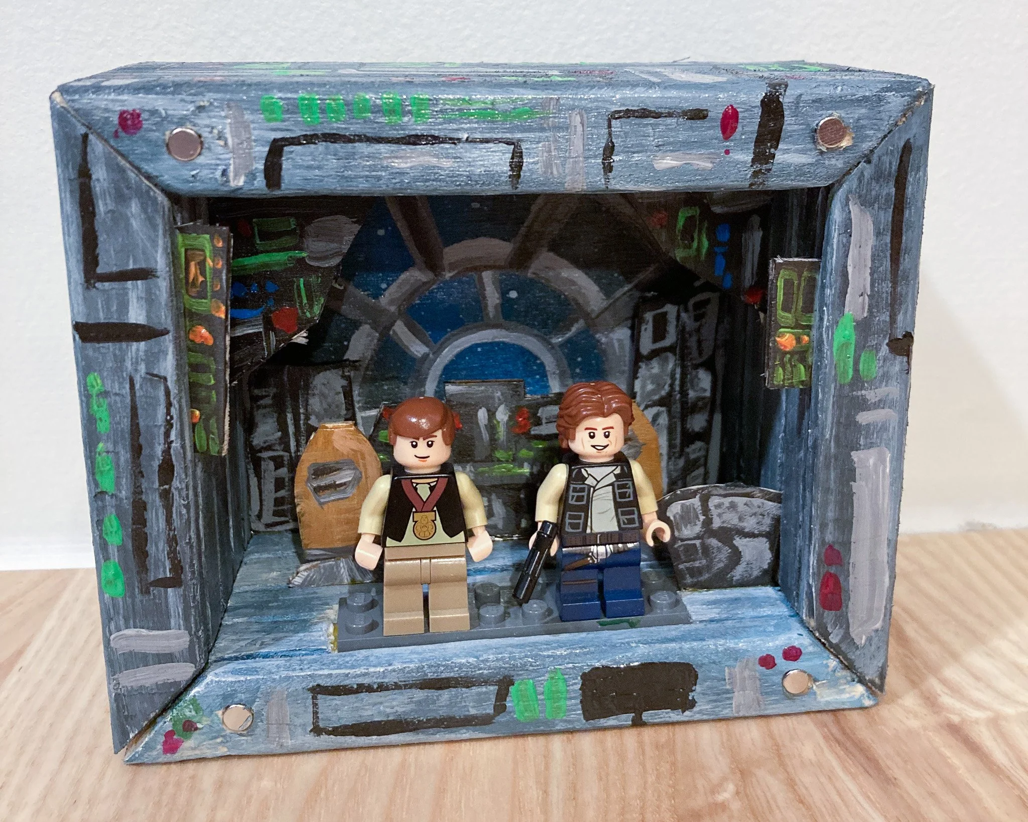 LEGO figures of two characters inside a painted backdrop resembling a sci-fi or spaceship interior.