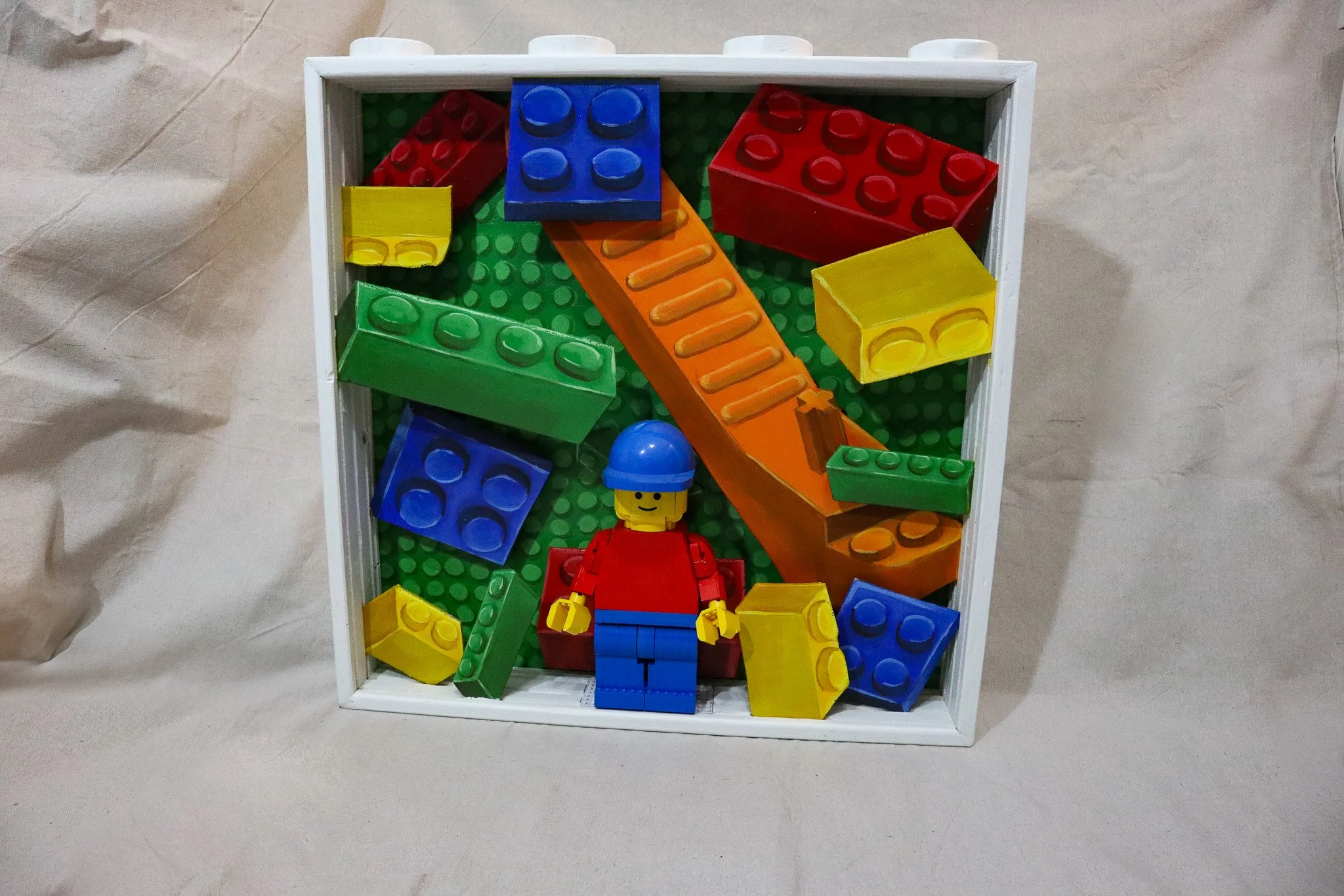 A toy display box with a LEGO minifigure and colorful building blocks arranged inside.
