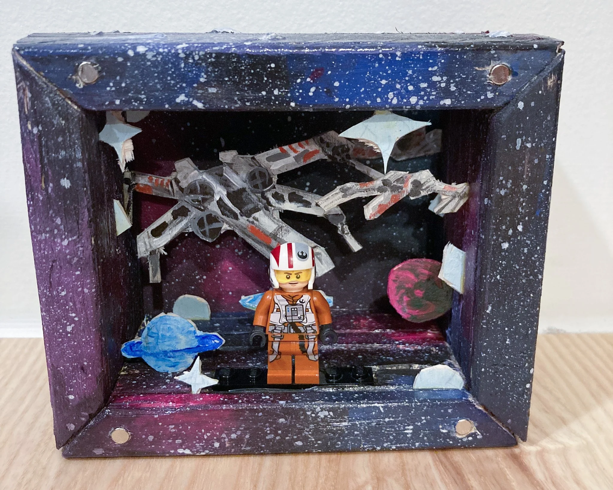 LEGO Star Wars diorama featuring a minifigure of Poe Dameron in front of a space background with a spacecraft and planets.