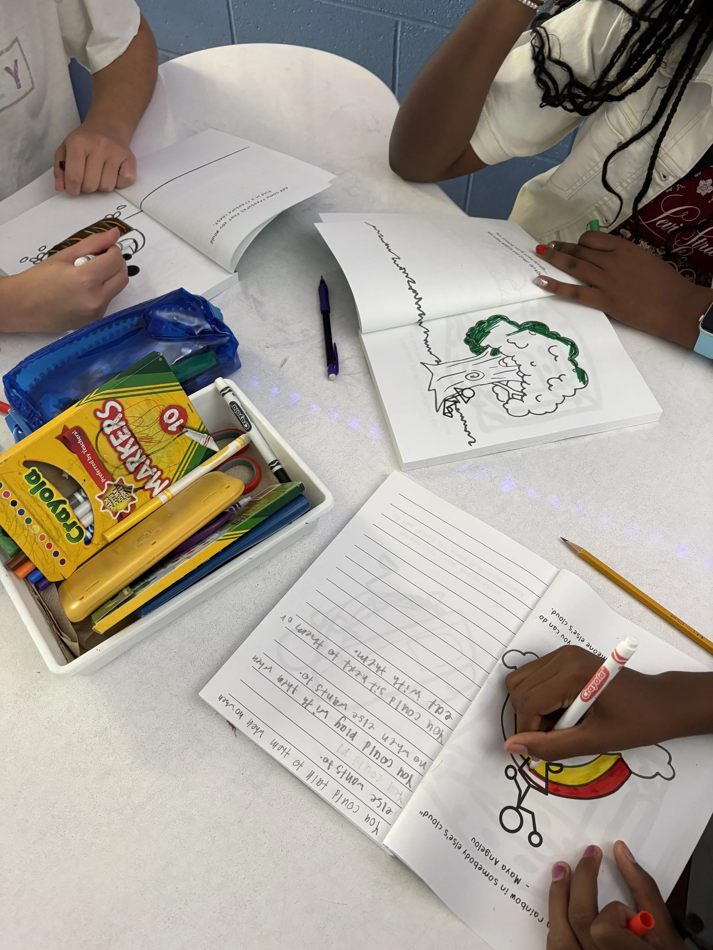 Children working on coloring and writing activities at a table with markers, colored pencils, and notebooks, with one child coloring a balloon.