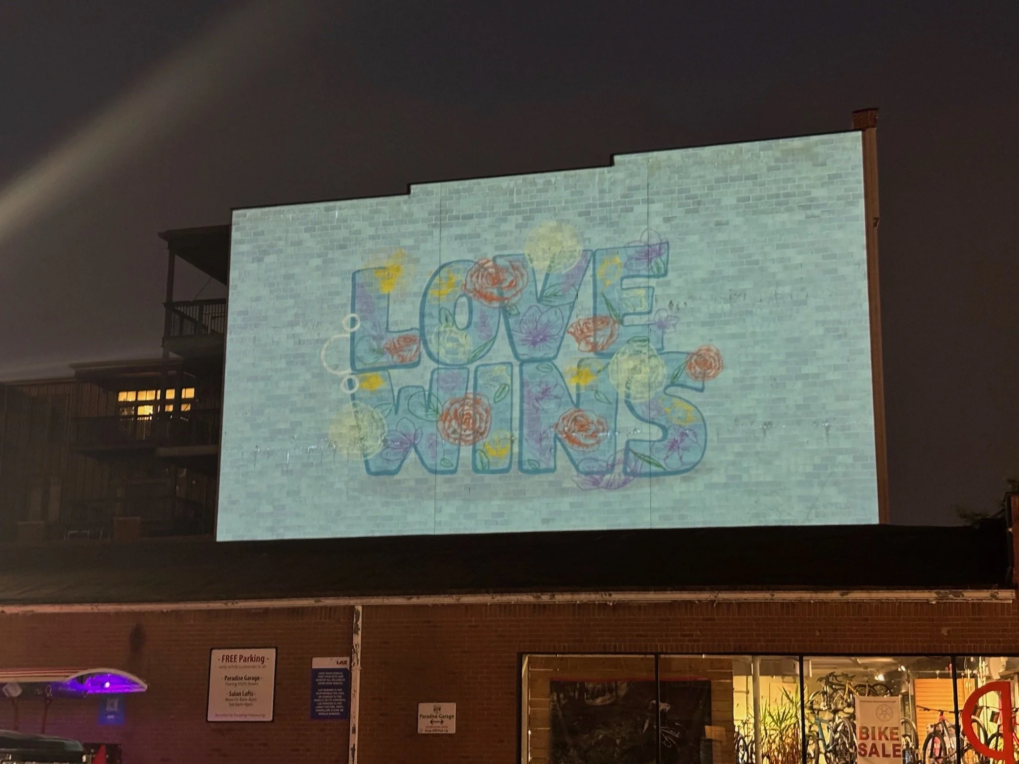 Projected image on the building wall spelling 'LOVE WINS' with colorful flowers and graphics.