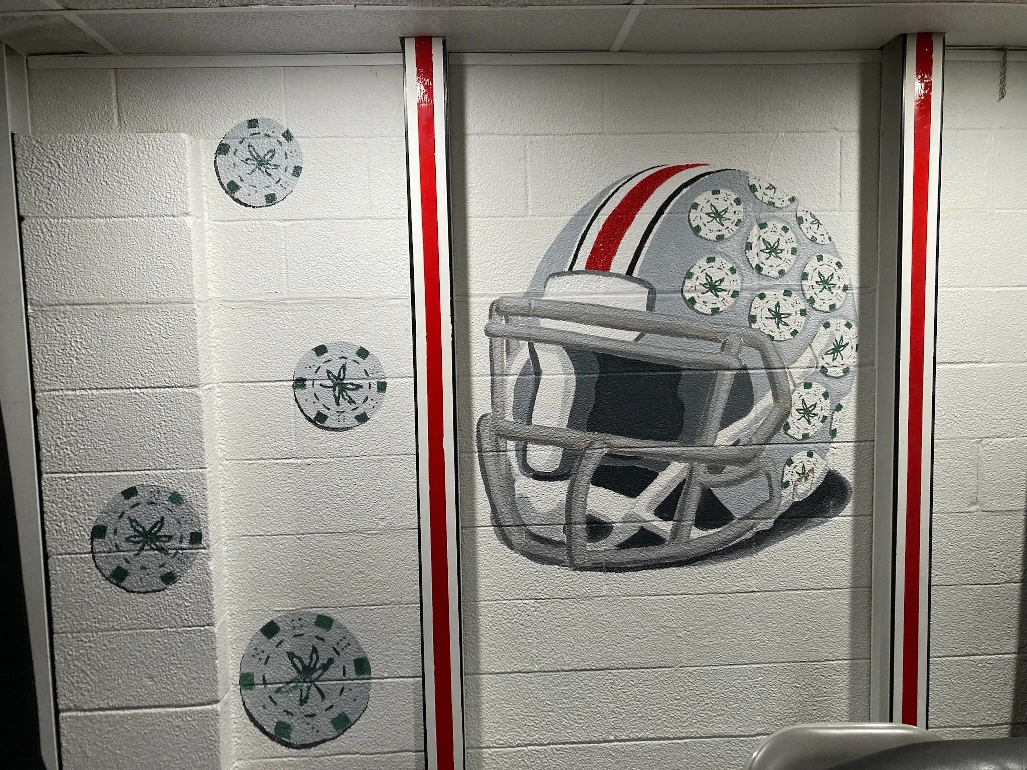 Wall mural of an Ohio State football helmet with a red stripe and a pattern of buckeye leaves on the side, painted on a cinder block wall