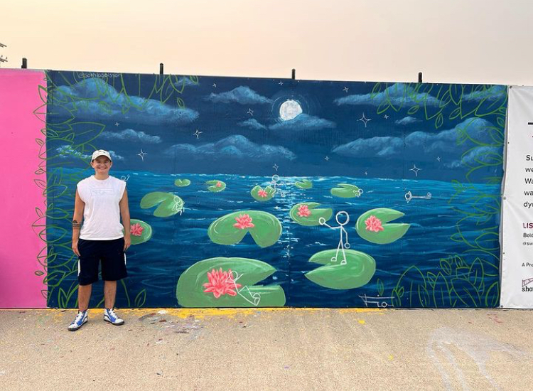 Person standing in front of a colorful mural of a night scene with lily pads, pink flowers, a full moon, and water under a starry sky.