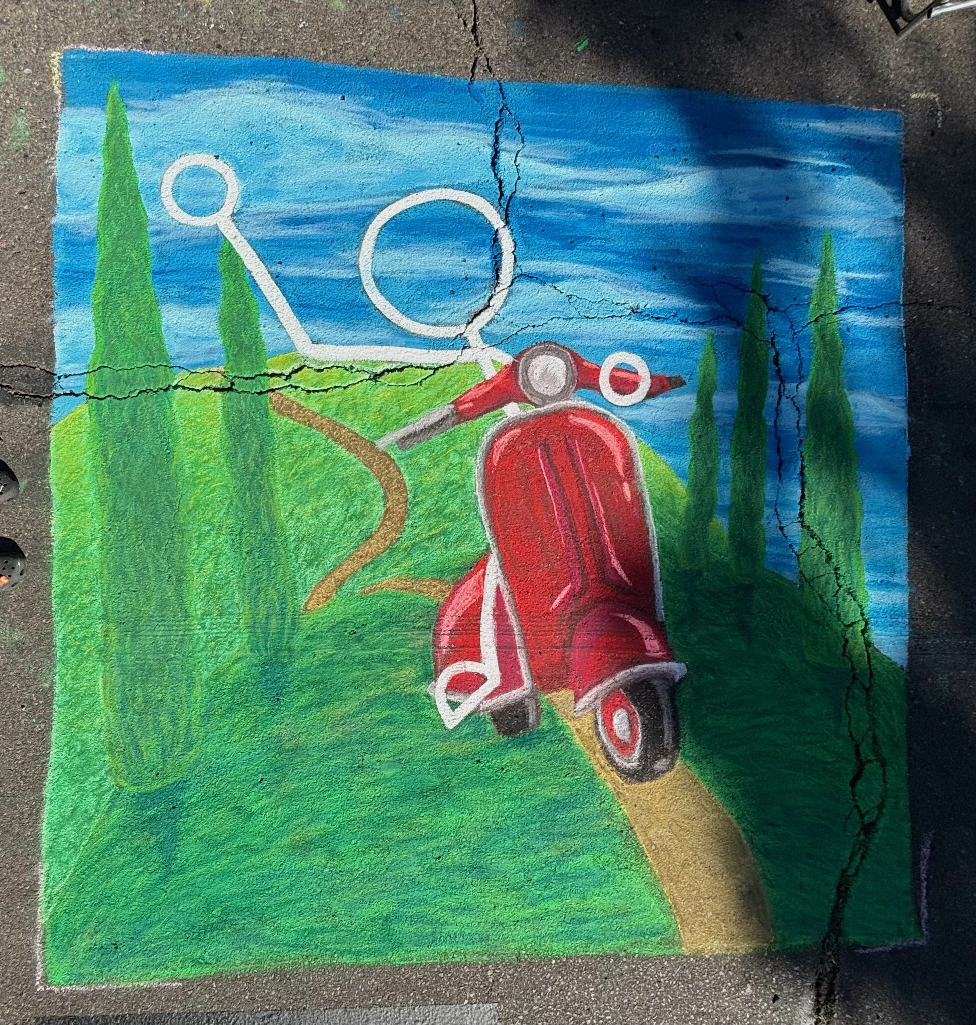 Colorful chalk mural of a red vespa on a winding yellow road with green hills, trees, and a blue sky with white clouds.