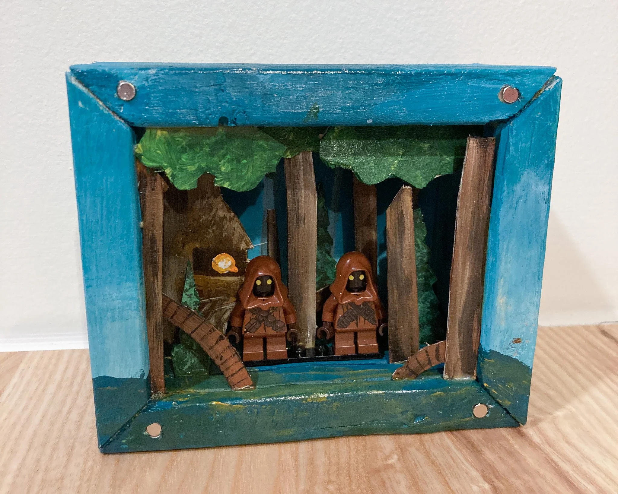 Lego scene of two brown characters with hoods in a forest backdrop with trees and greenery.