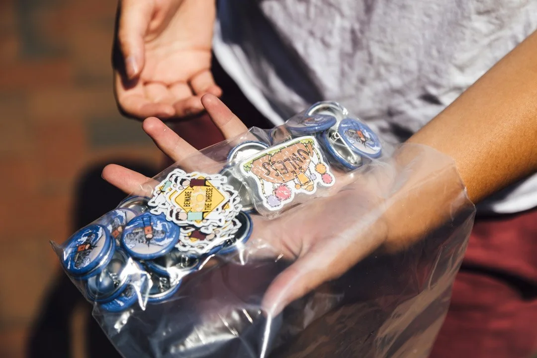 Person holding a plastic bag filled with round badges with cartoon and text designs.