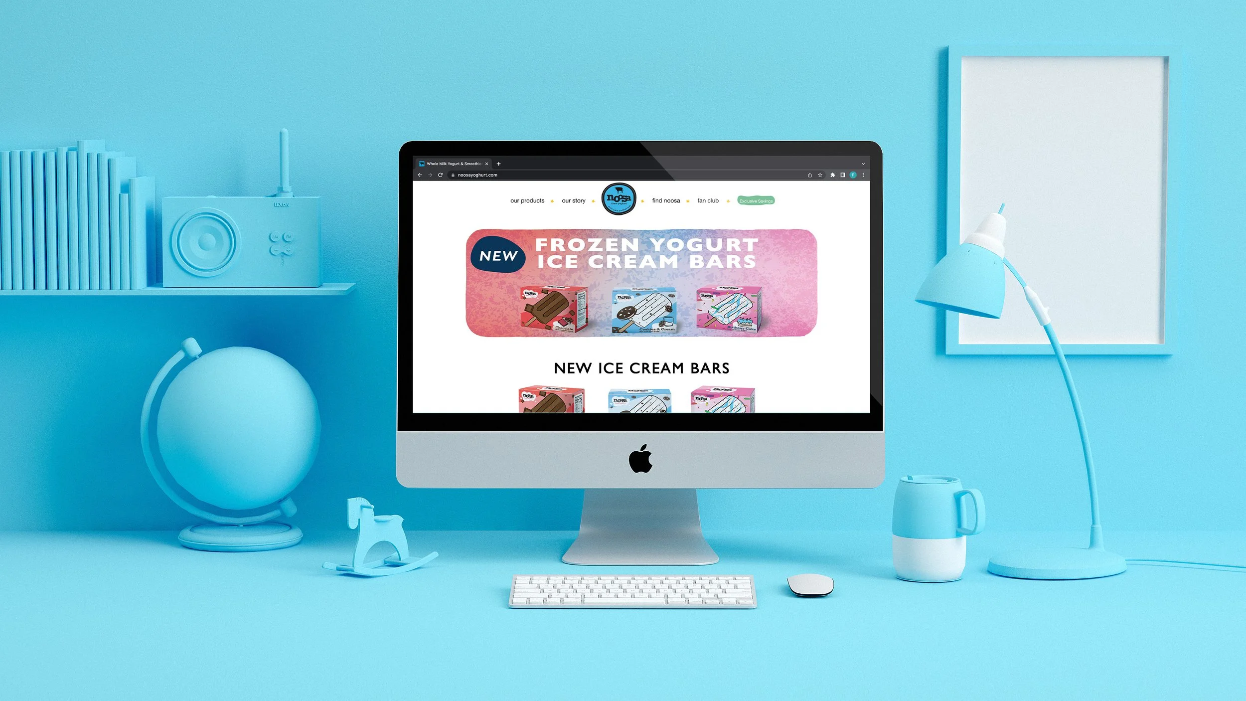 A computer on a blue desk displaying a website for Noosa Yoghurt promoting their new frozen yogurt ice cream bars, with blue desk accessories including a globe, a mug, a lamp, and a small rocking horse, against a blue wall with a shelf and a whiteboard.