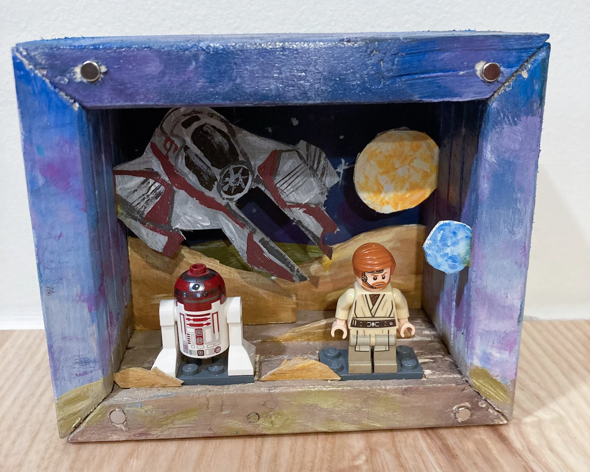 Handmade diorama featuring LEGO figures of BB-8 and Luke Skywalker from Star Wars, with a painted painted space background, including planets and a spaceship.