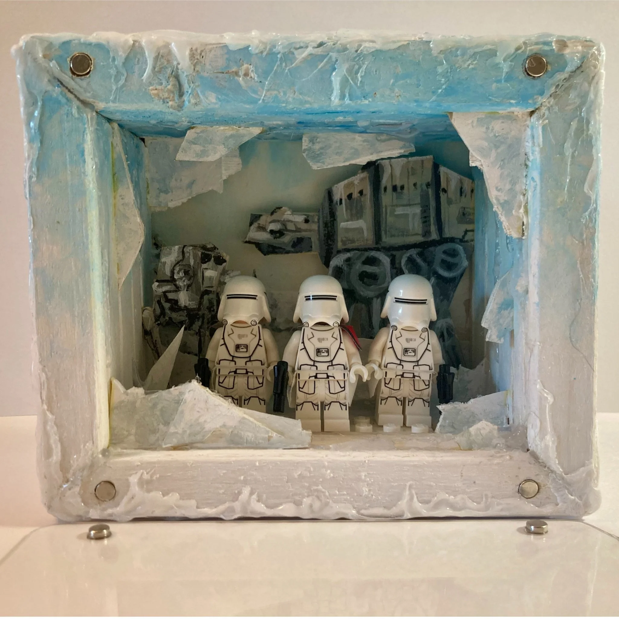 A diorama with LEGO stormtroopers inside a painted styrofoam frame, showcasing a snowy, icy landscape with buildings and ruined structures in the background.