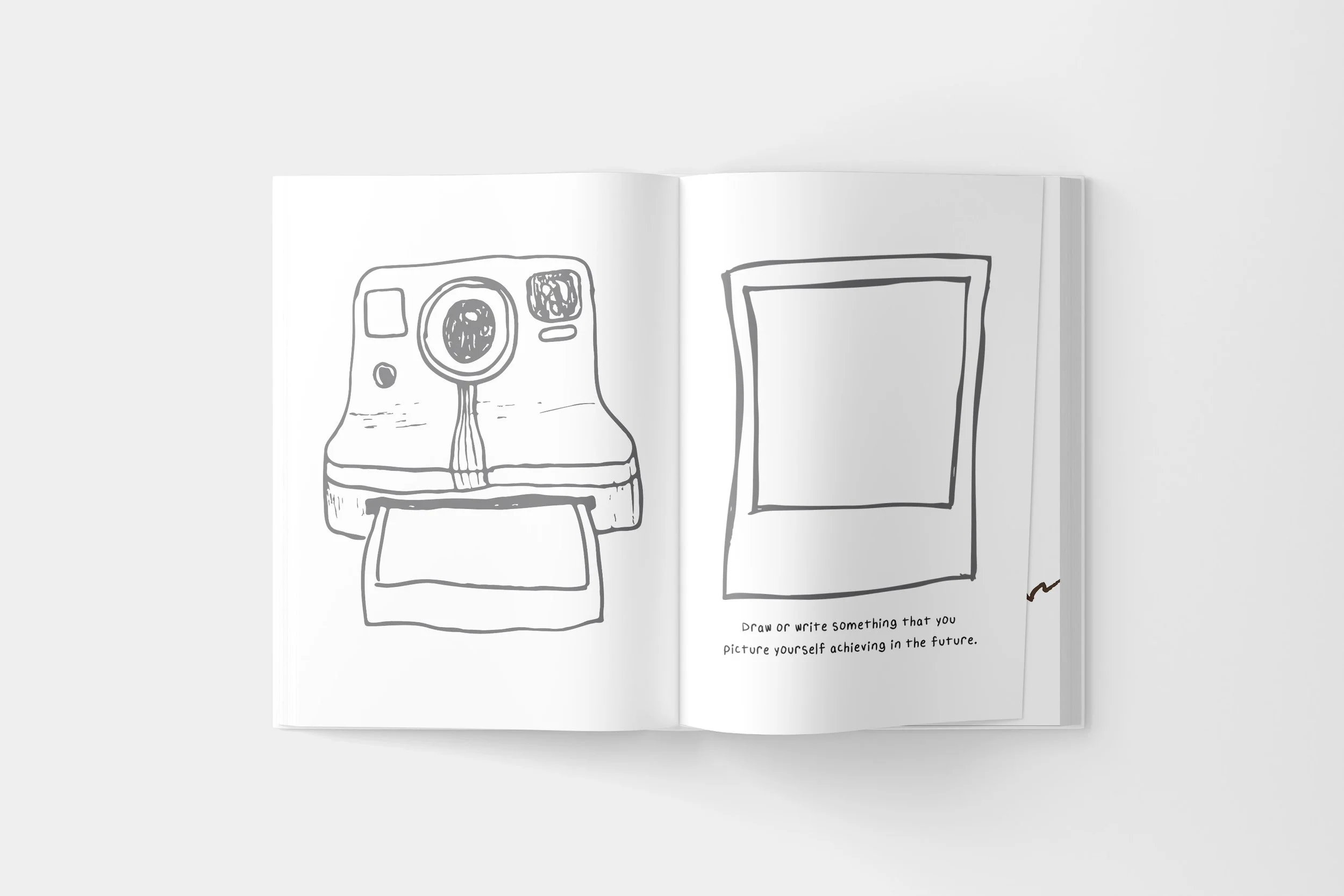Open sketchbook with drawings: a polaroid camera on the left page and a blank picture frame on the right page, with the prompt to draw or write what you picture yourself achieving in the future.