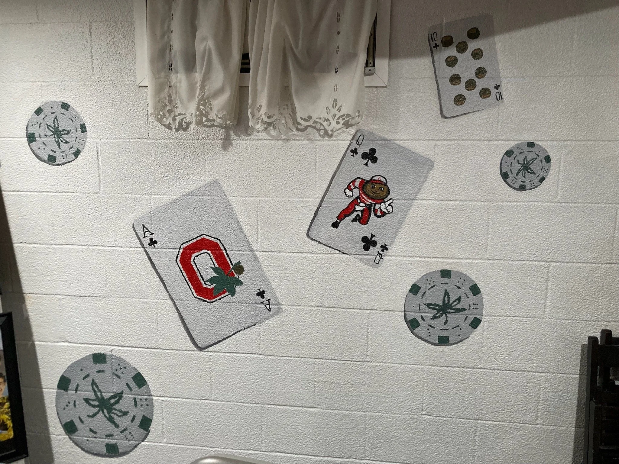 Wall decorated with playing cards, poker chips, and a white window curtain above.