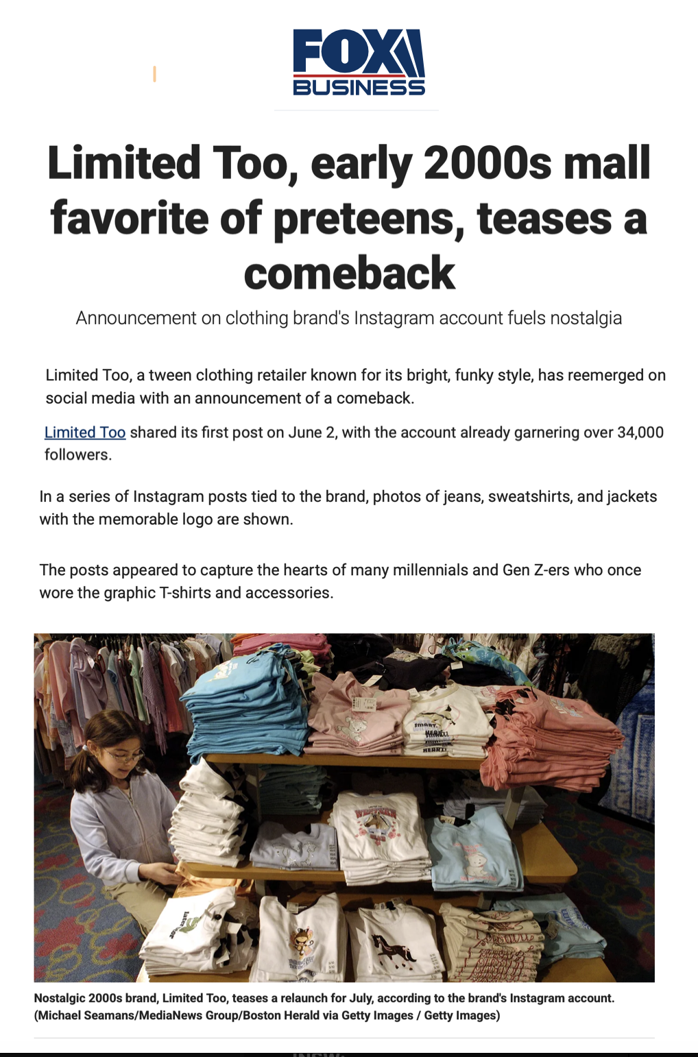A young girl with glasses and a white hoodie looking at folded clothes on a display table in a retail store, with racks of clothing behind her.