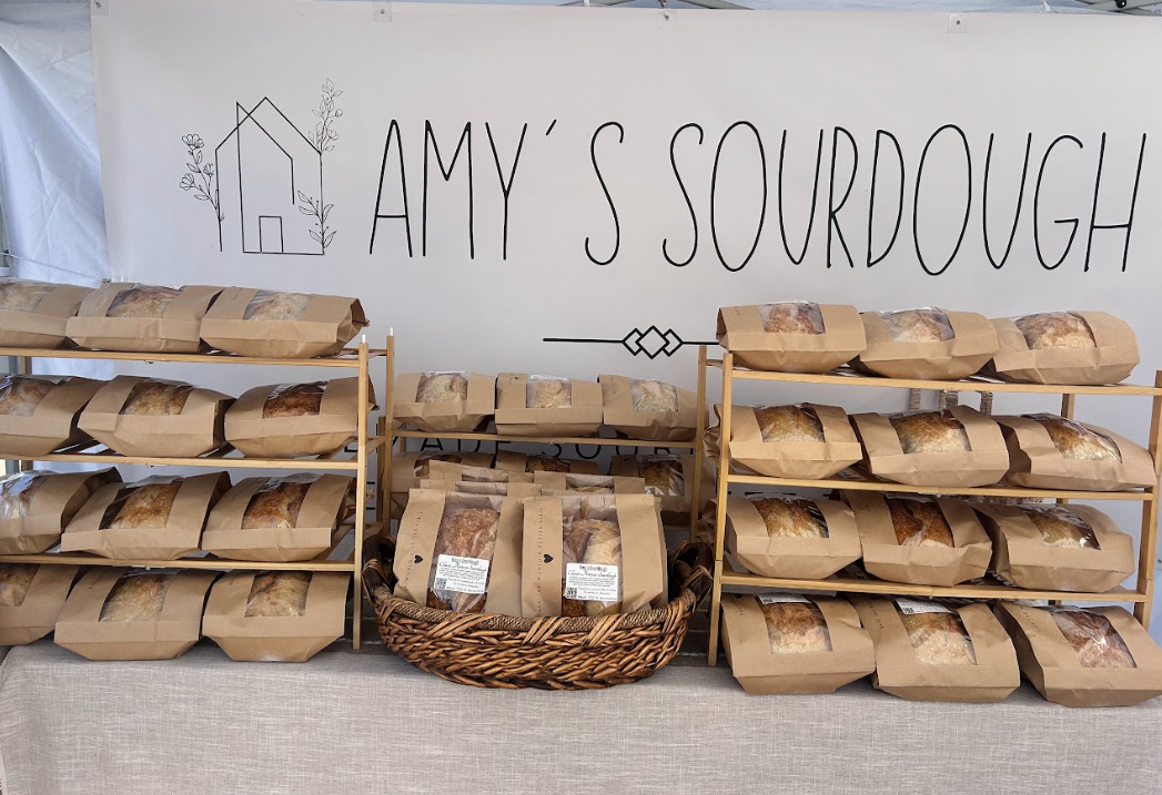 Display of sliced sourdough bread in paper bags on wooden shelves and a basket, at Amy's Sourdough booth.