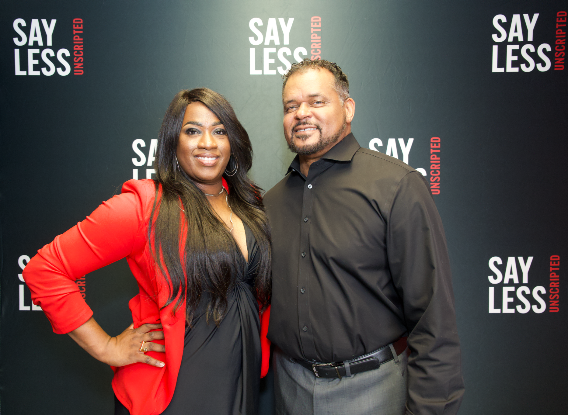 Say Less Unscripted co-hosts Milton Quinn and Jacquelyn Clayborn standing together in front of the podcast backdrop.