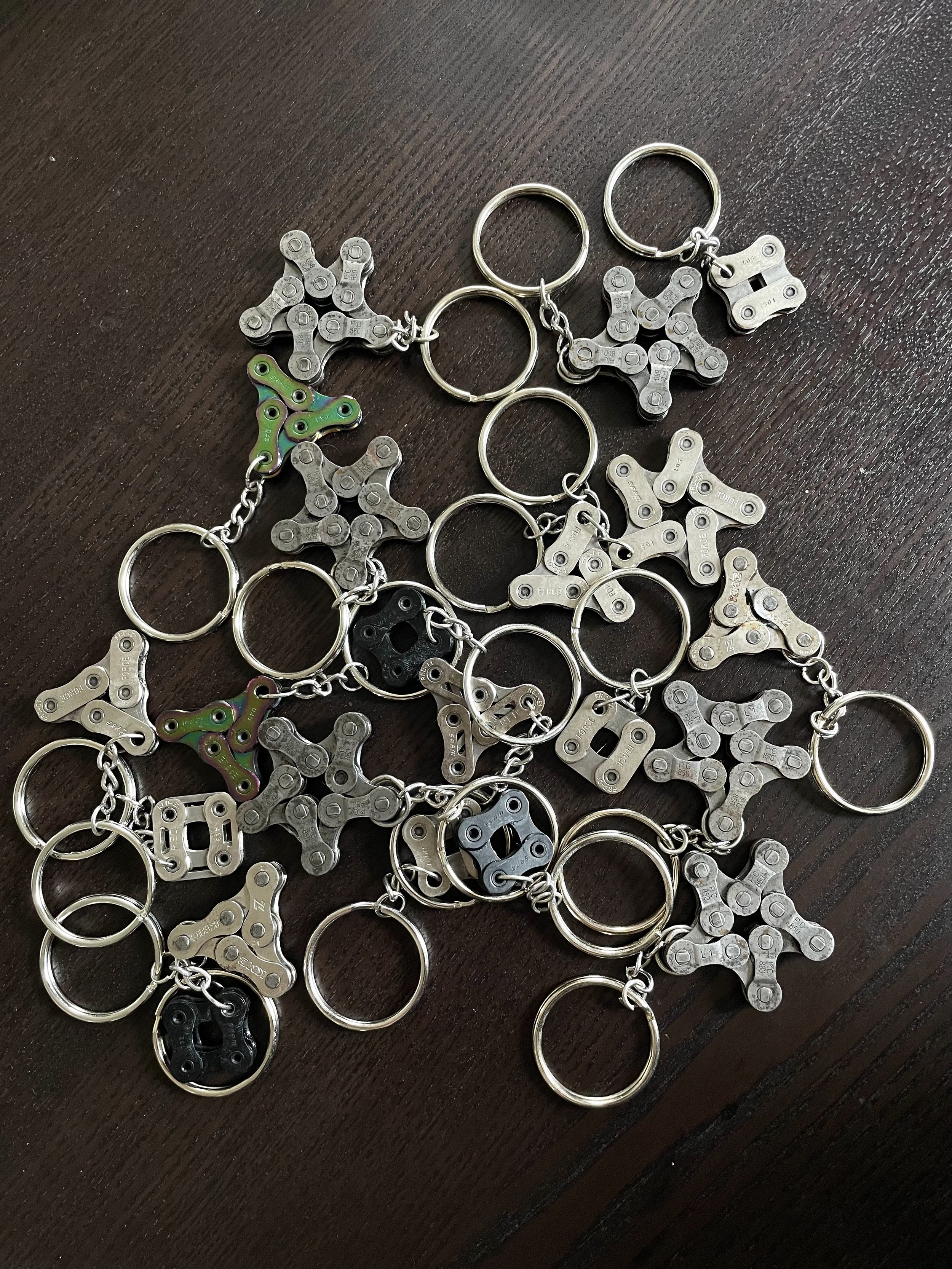 A pile of keychains featuring miniature fidget spinners made from metal and plastic, scattered on a dark brown wooden surface.