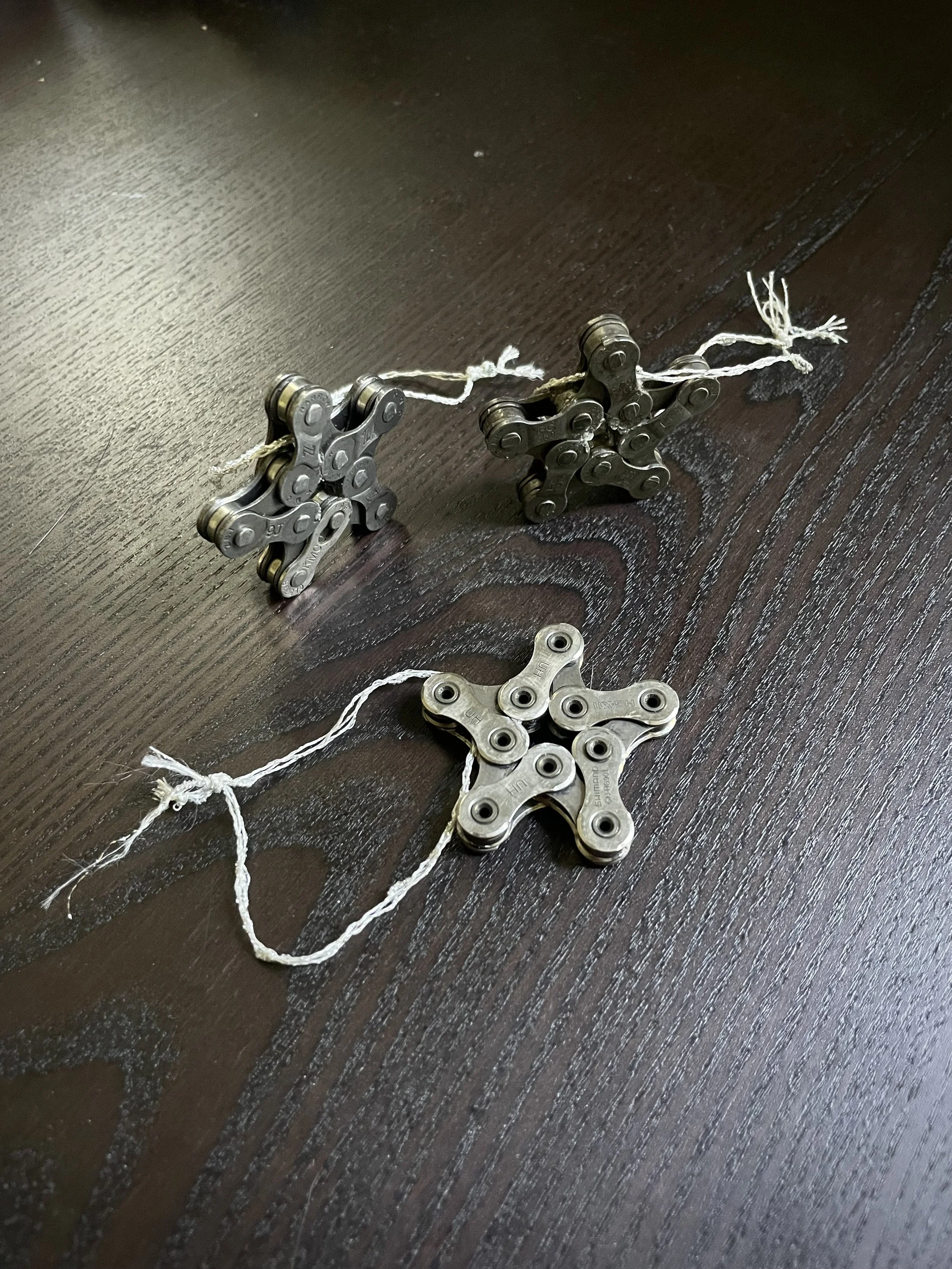 Two star-shaped clusters of metal roller chain links connected by a string, with a single loose metal chain link in front on a dark wooden surface.