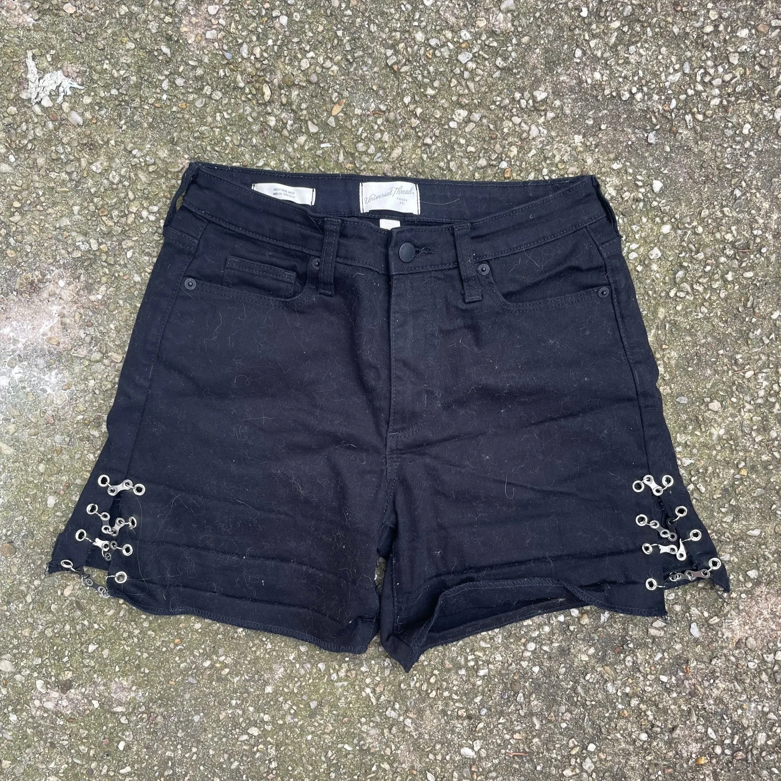 Black denim shorts with lace-up detail on the sides, lying on a gravel surface