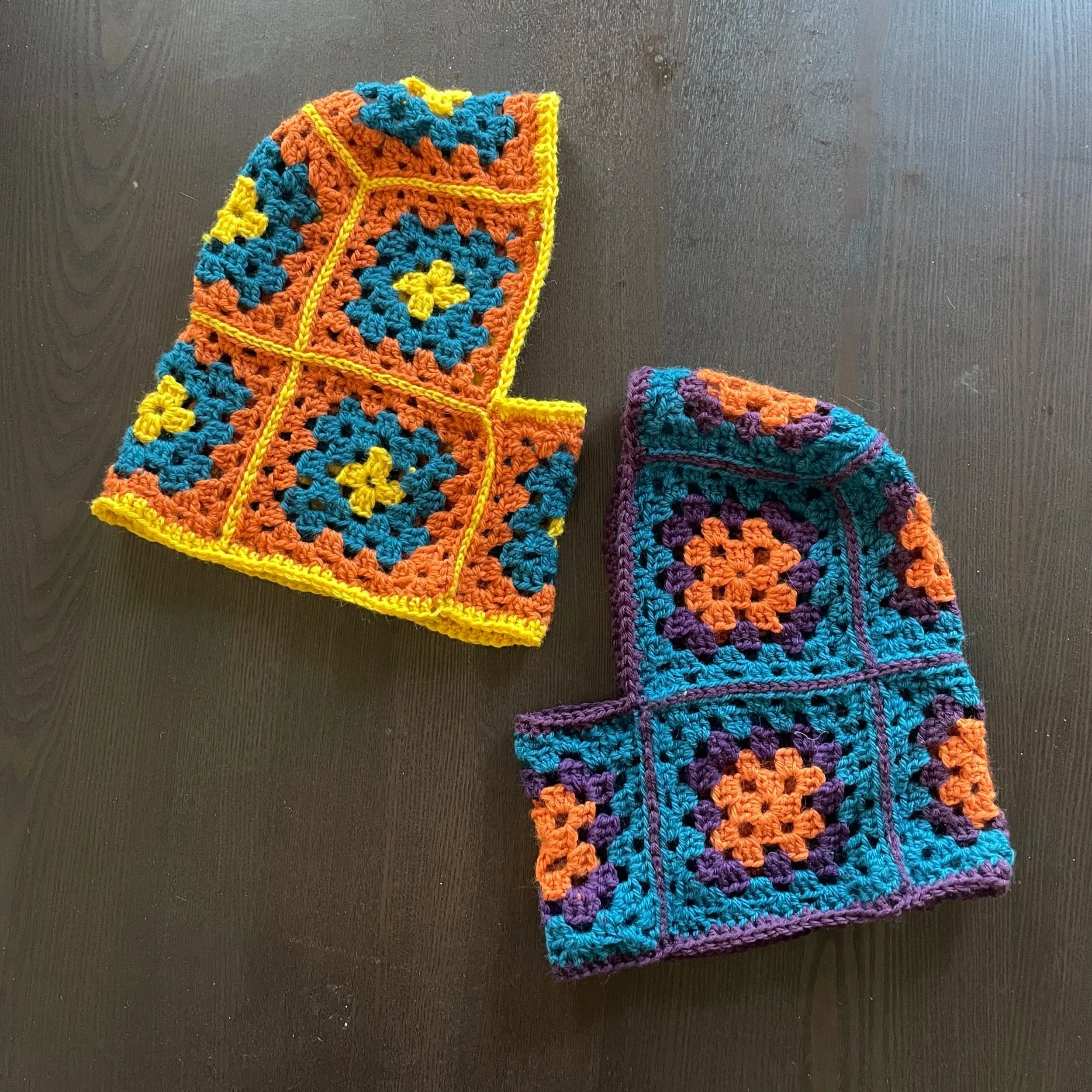 Two colorful crocheted squares with floral patterns, one yellow and orange, the other purple and orange, on a dark surface.