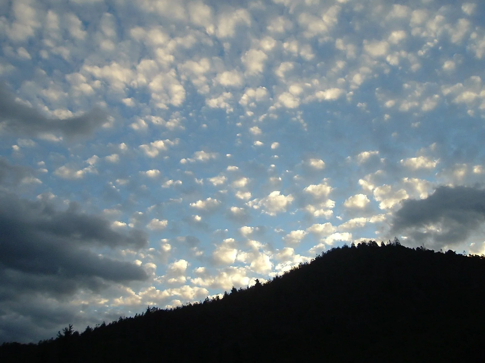 Sky filled with scattered clouds above a dark silhouette of a mountain.